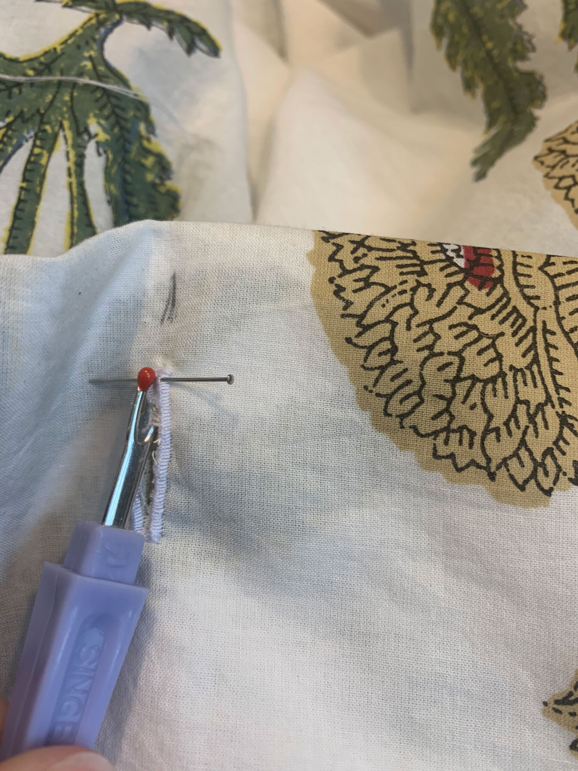 using a seam ripper to cut the fabric inside the button hole with a pin to stop the seam ripper from going too far