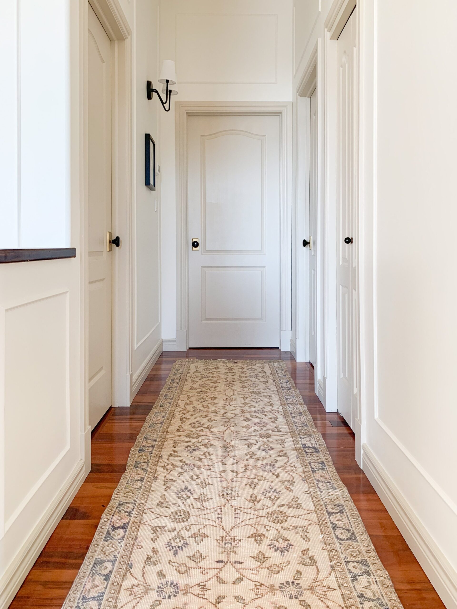 Beige vintage runner in a hallway with lots of doors painted edgecomb grey and walls white, with brass and black doorknobs