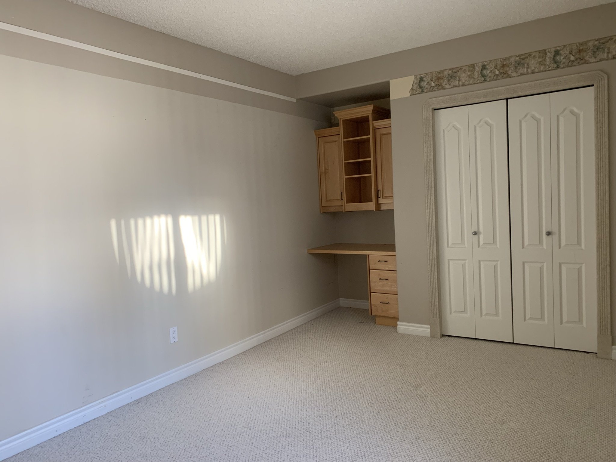 empty guest room with a built in maple desk with a staggered top and wallpaper border partially removed