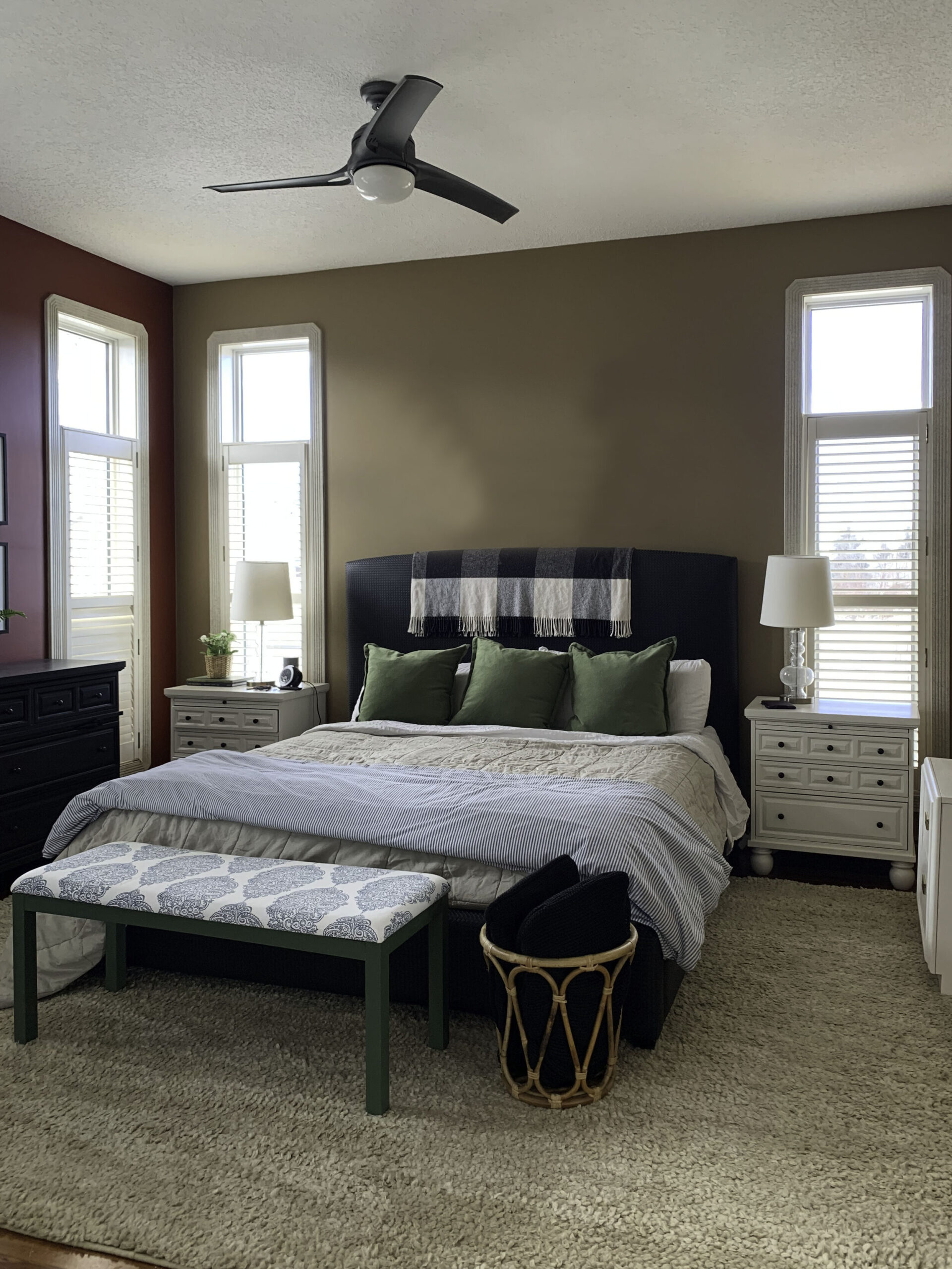 bedroom with brown walls, two windows, black bed and bench at the foot of the bed