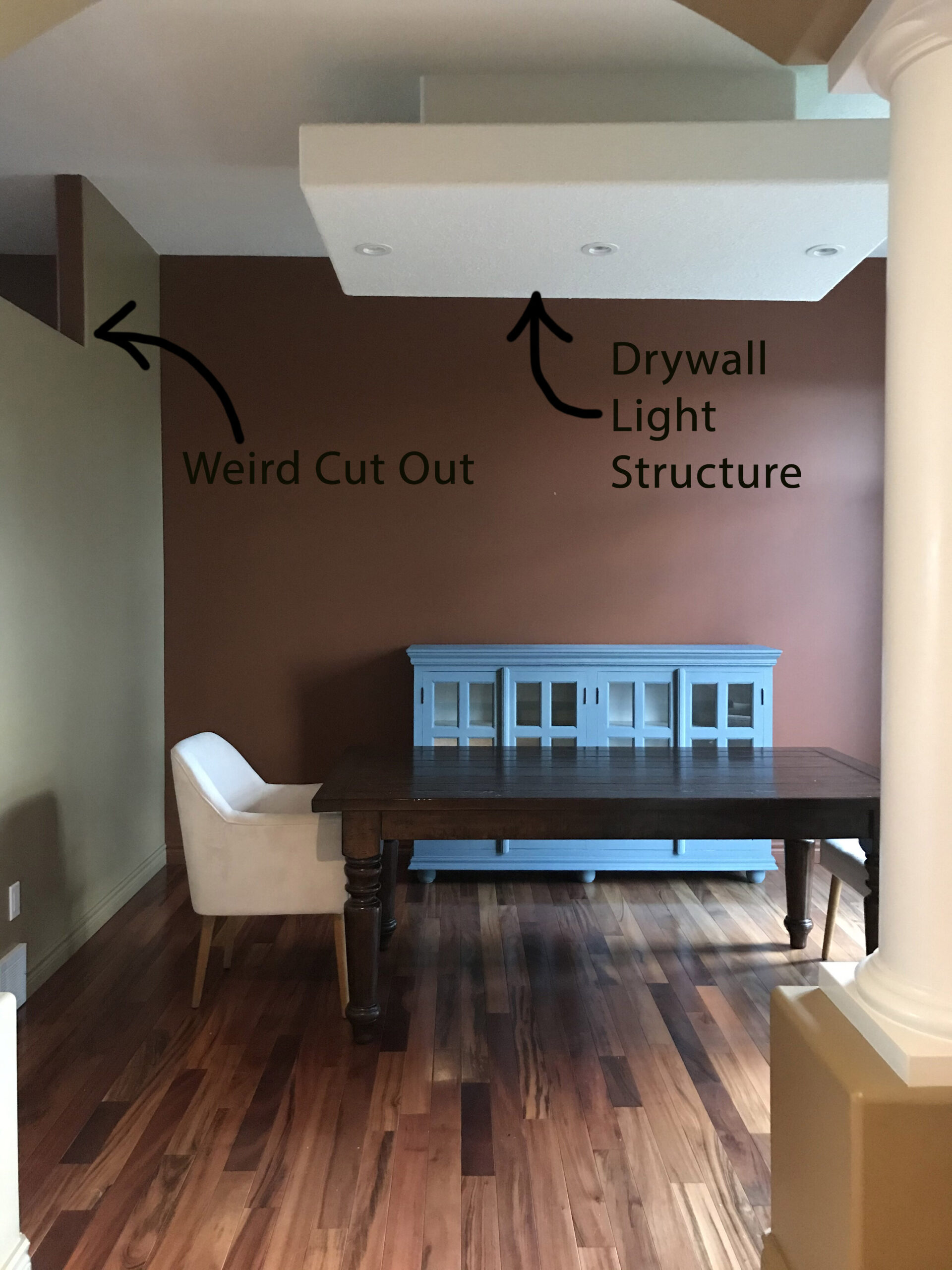 Dining room with minimal furniture with text indicating "weird cut out" with an arrow pointing to a hole in the wall on the left, and "drywall light structure" pointing to a box on the ceiling that is constructed out of drywall with pot lights in it
