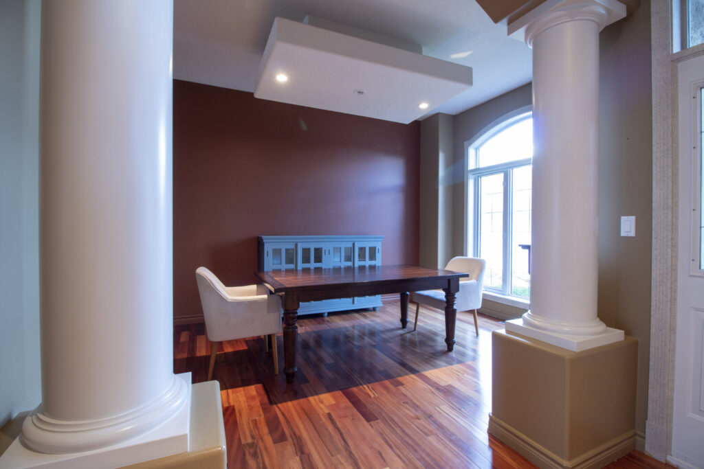 photo of a dining room with brown walls, arched opening with columns, minimal furniture, wood floors