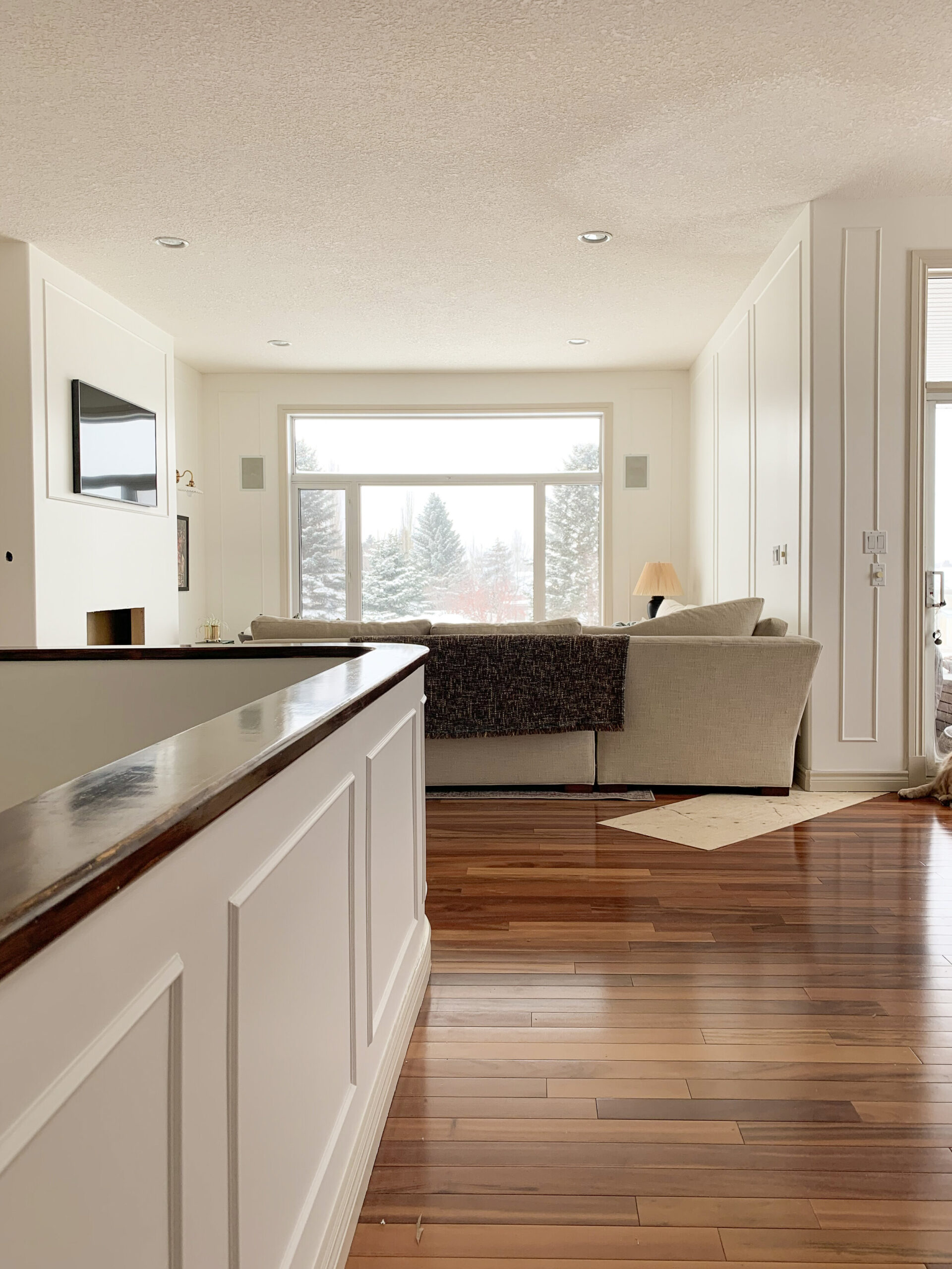 Living room with white walls, large bare window, fireplace partially constructed and a large sectional, box moulding