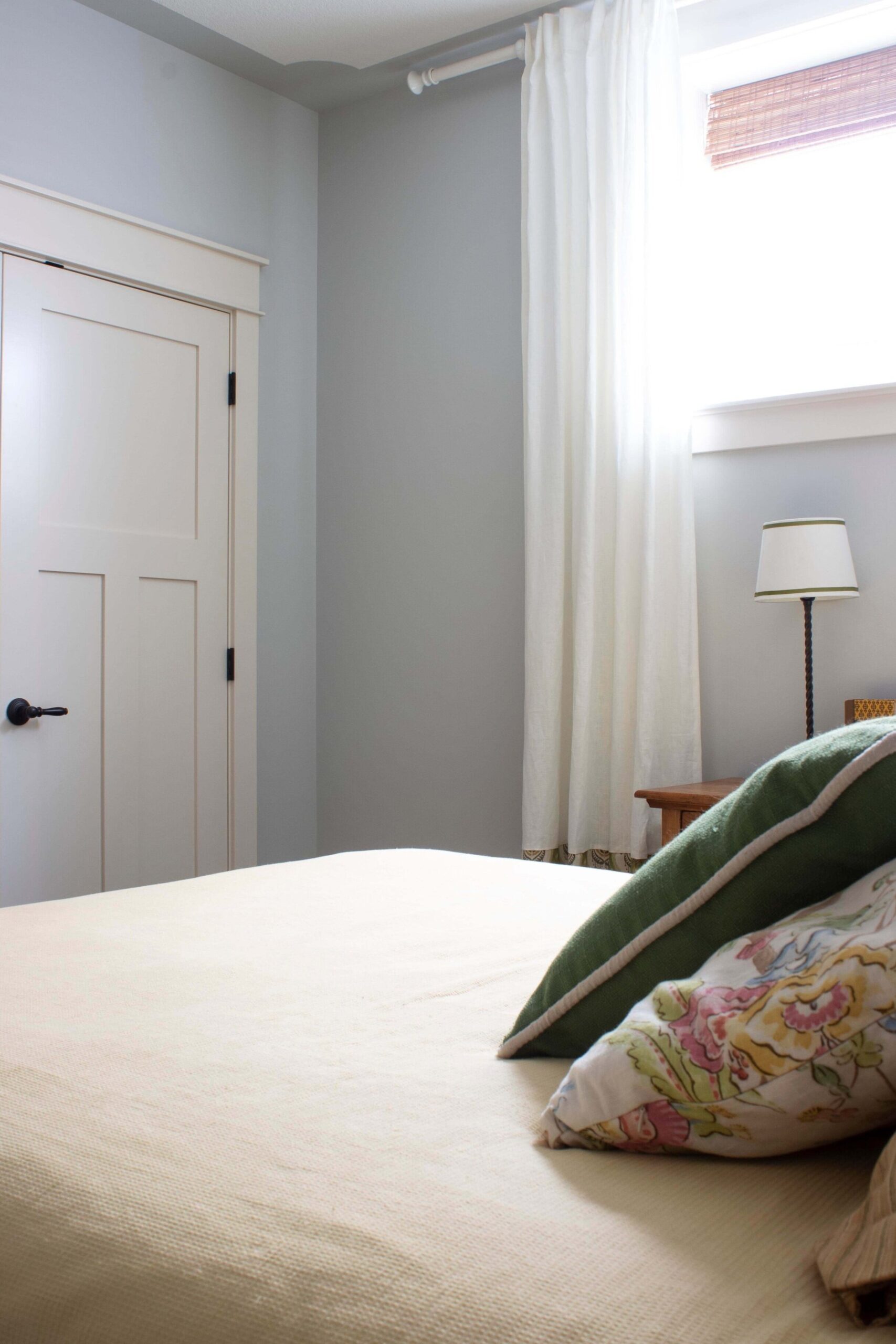 View over bed with white closet doors in background, grey walls, white curtains, green and floral pillows on bed