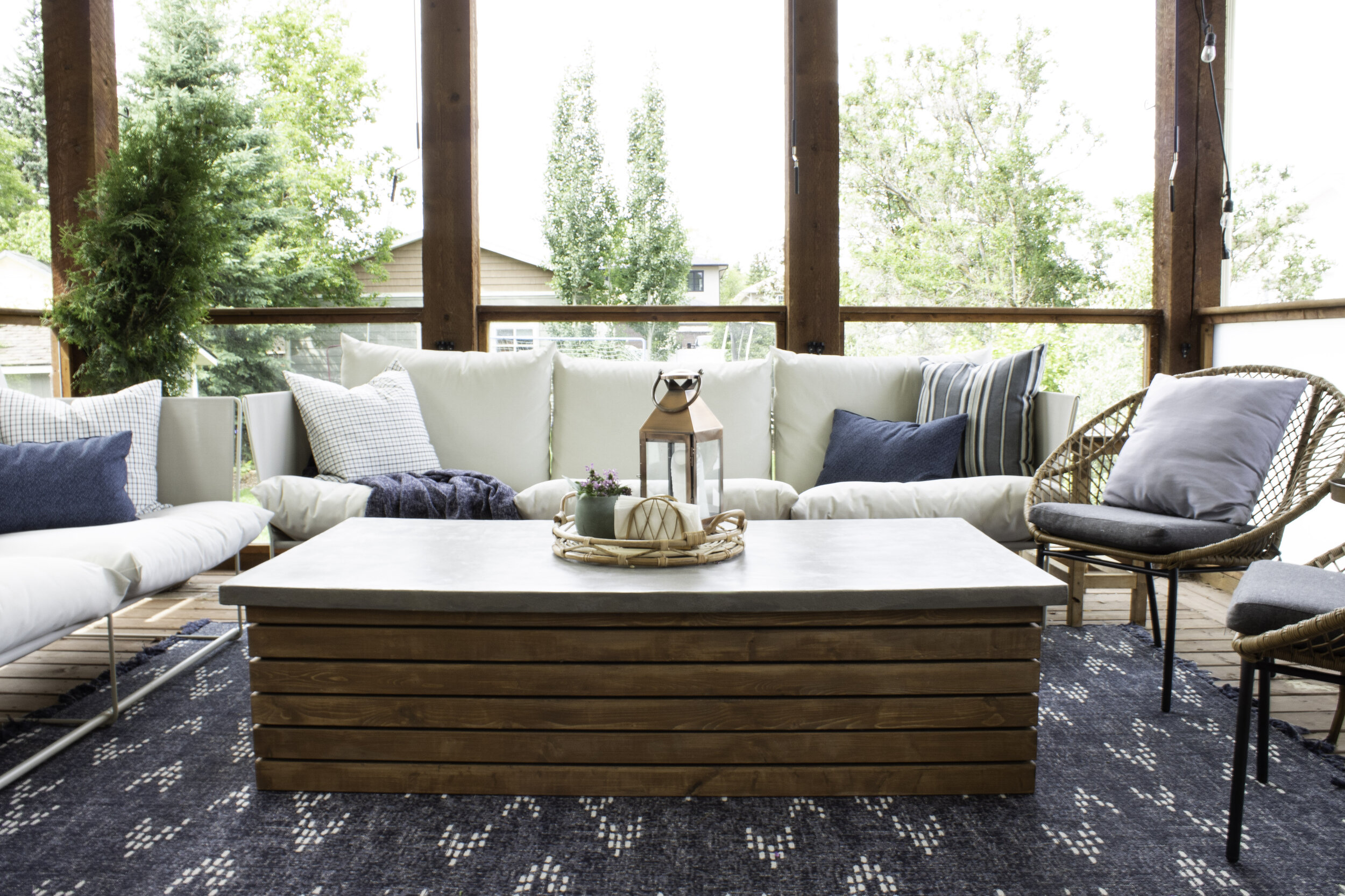 outdoor patio with outdoor couches, blue outdoor rug, wicker end chairs, and a concrete topped outdoor table with wood slats