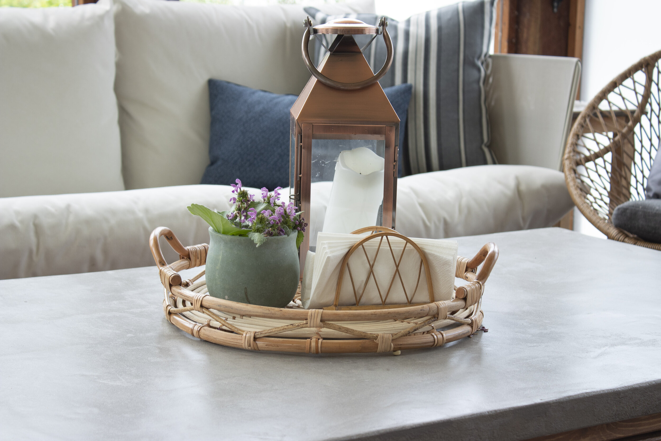 concrete coffee table top close up with wicker tray with lantern and plant and couches in the background