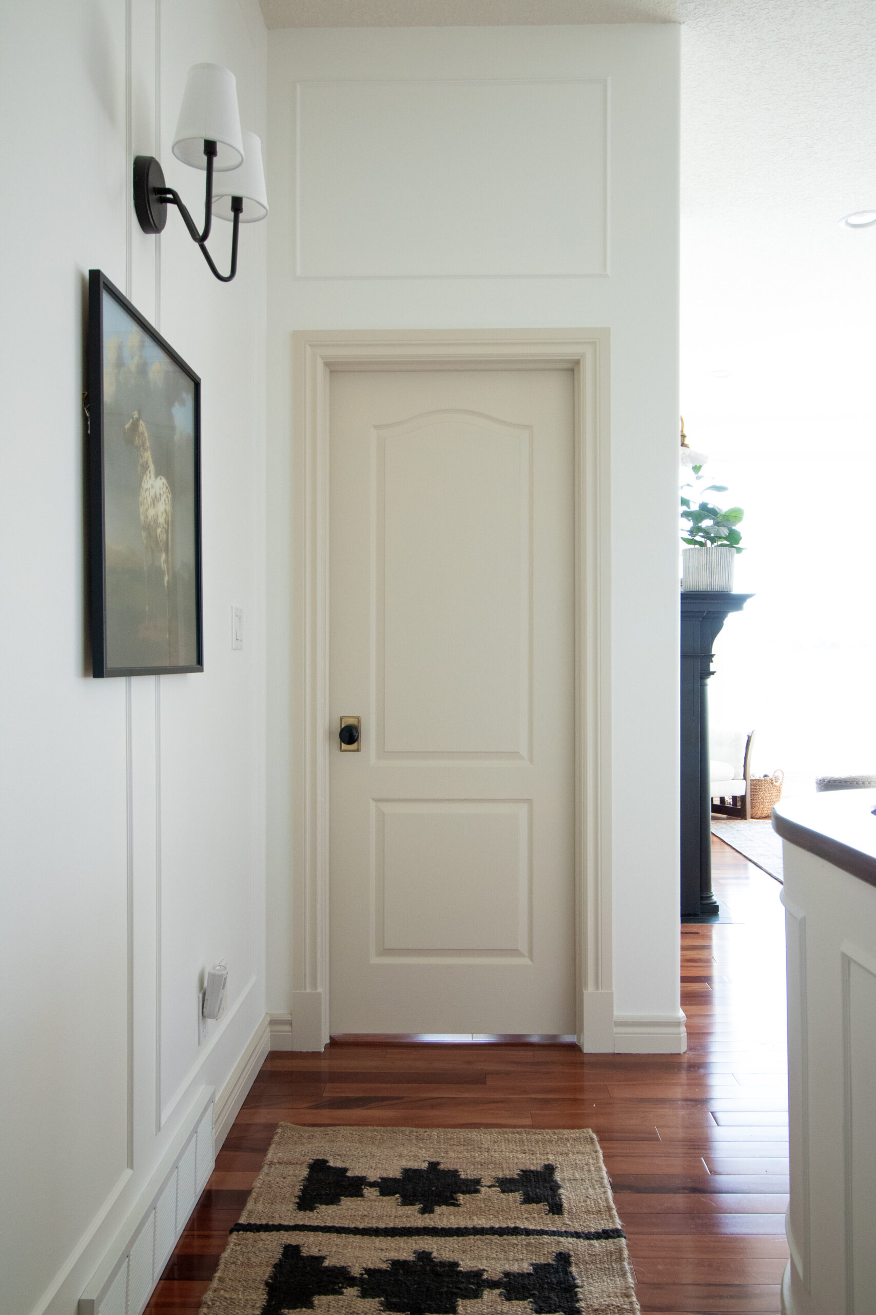 door showing box trim moulding installed above the door in line with the door casing even though that is not centered on the wall.  Jute runner and white walls with contrast trim 