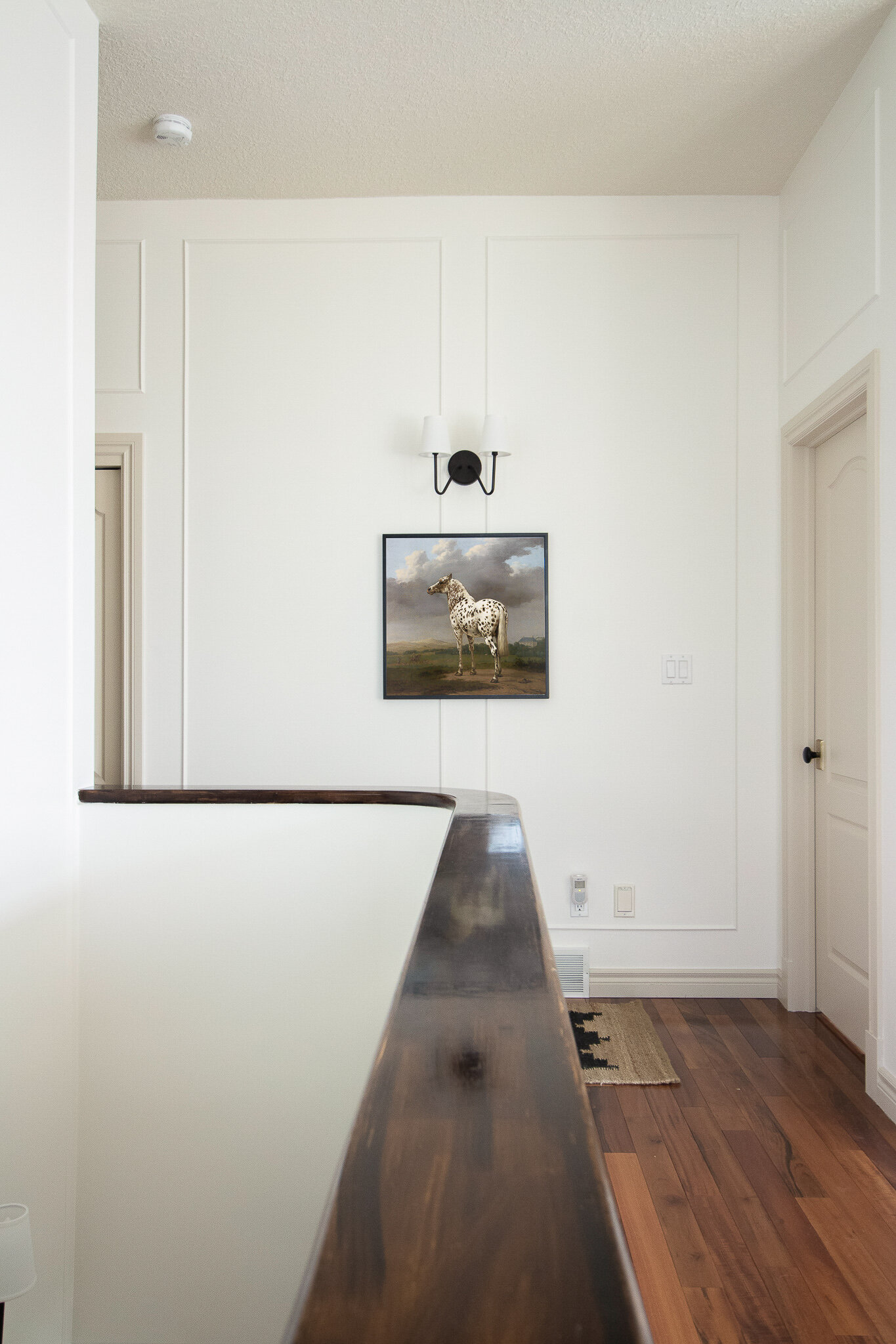 looking along the top of a staircase pony wall with wood top, box trim moulding on walls with vintage horse art and black two armed sconce