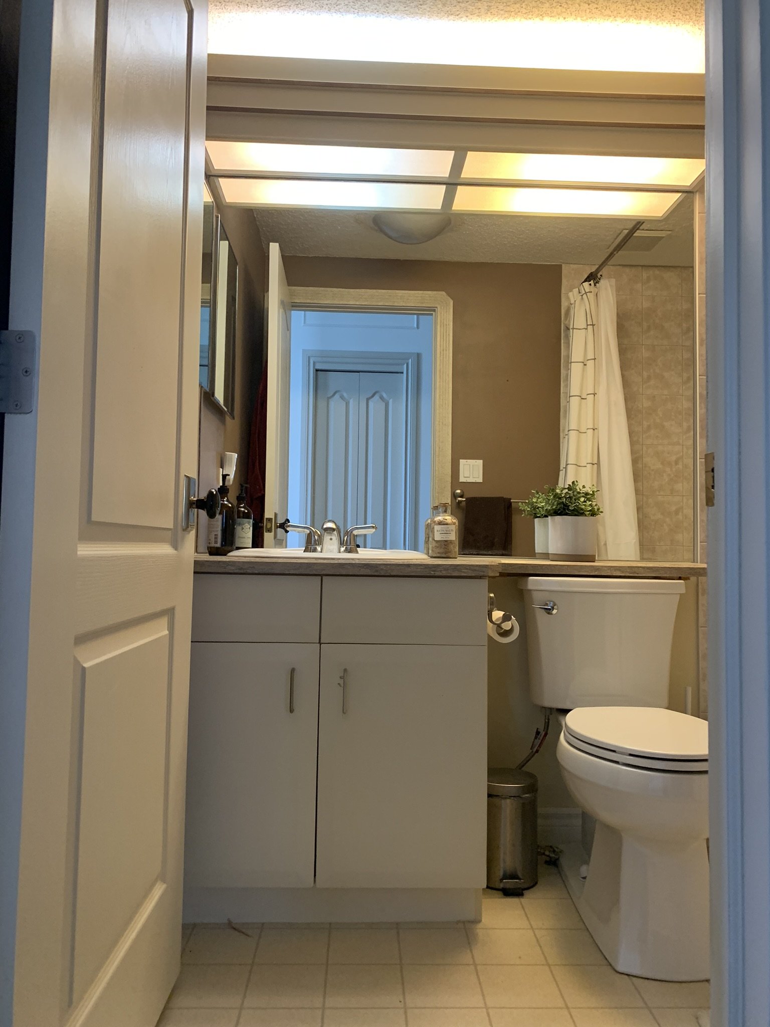 Bathroom before demolition with a large wall mirror, flourescent light and laminate counters