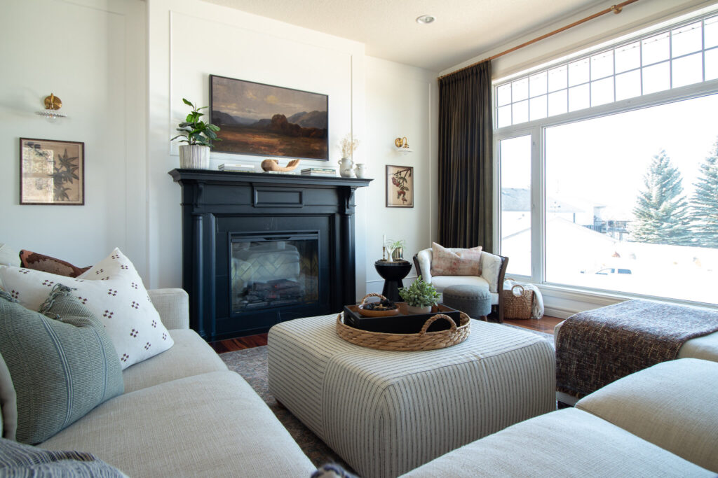 Modern traditional living room with black antique mantel, Black marble surround, white walls with contrasting beige trim, green velvet curtains and a large window 