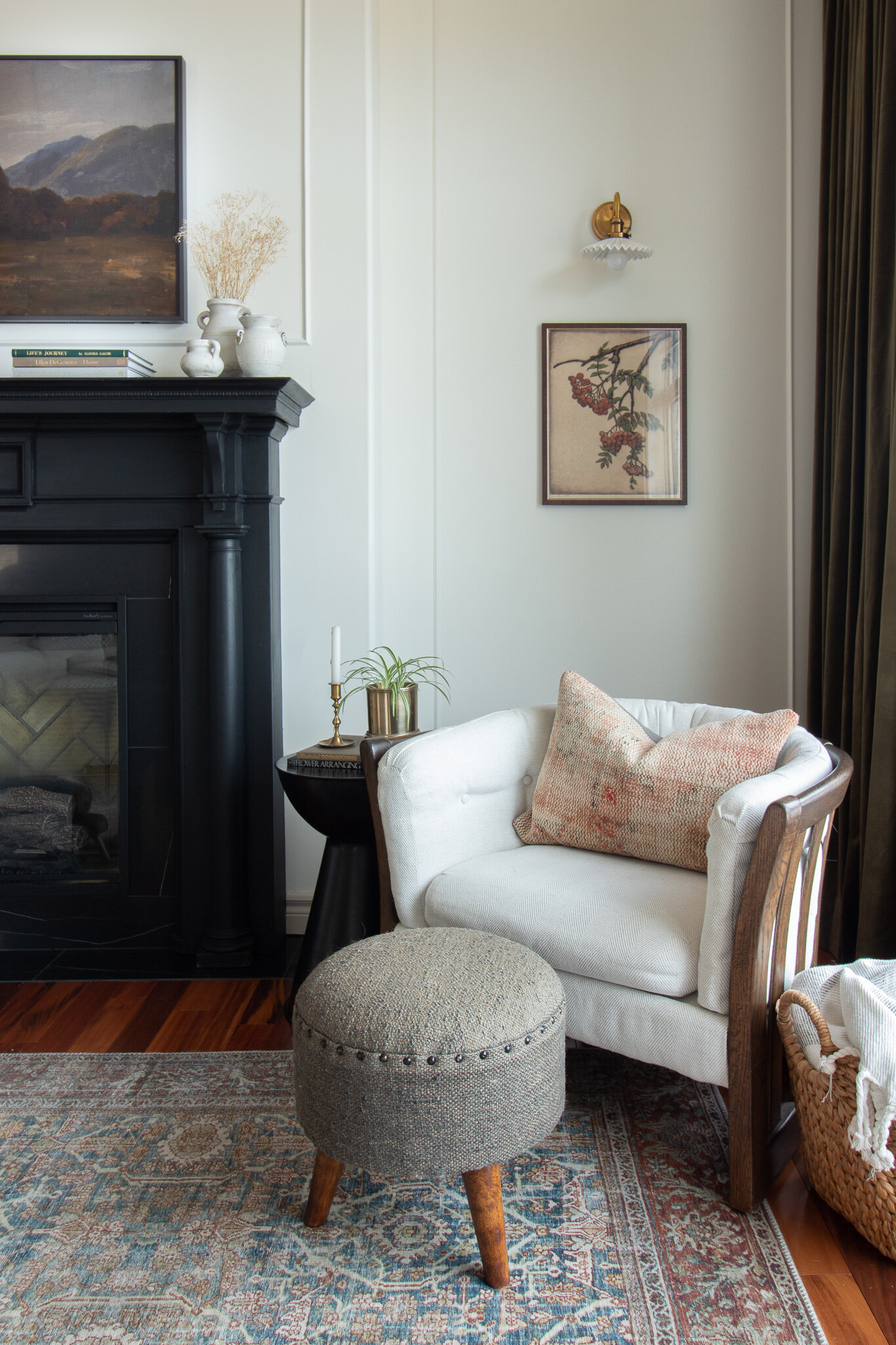 corner of living room with vintage oak chair, modern blue stool, vintage style rug, white and brass ceramic sconce, black antique fireplace, vintage style art and green velvet curtains