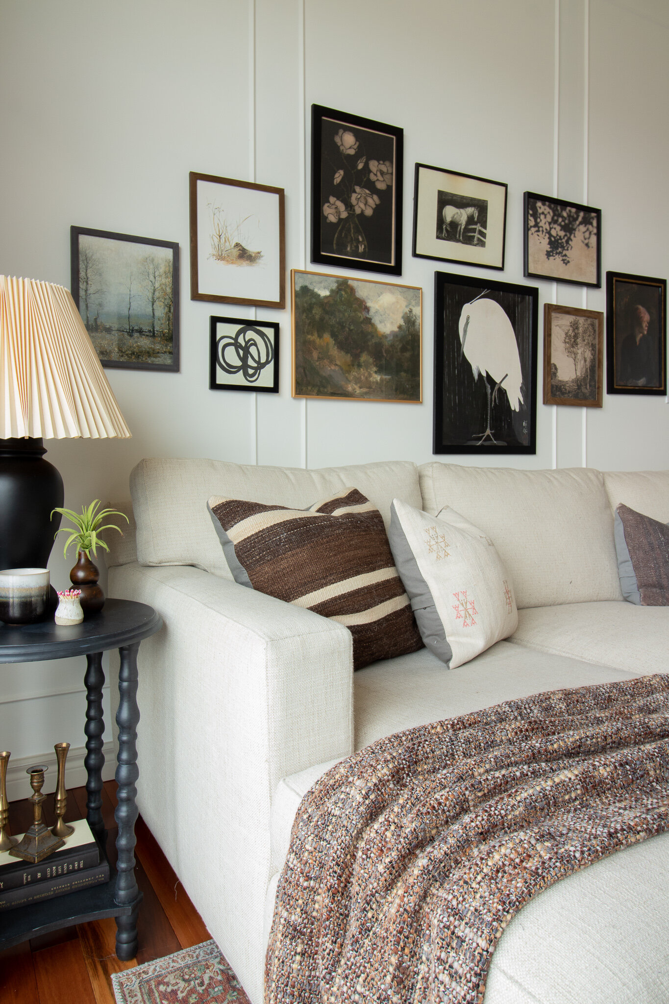 gallery wall of vintage art, sectional couch with pillows, side table with lamp and accessories