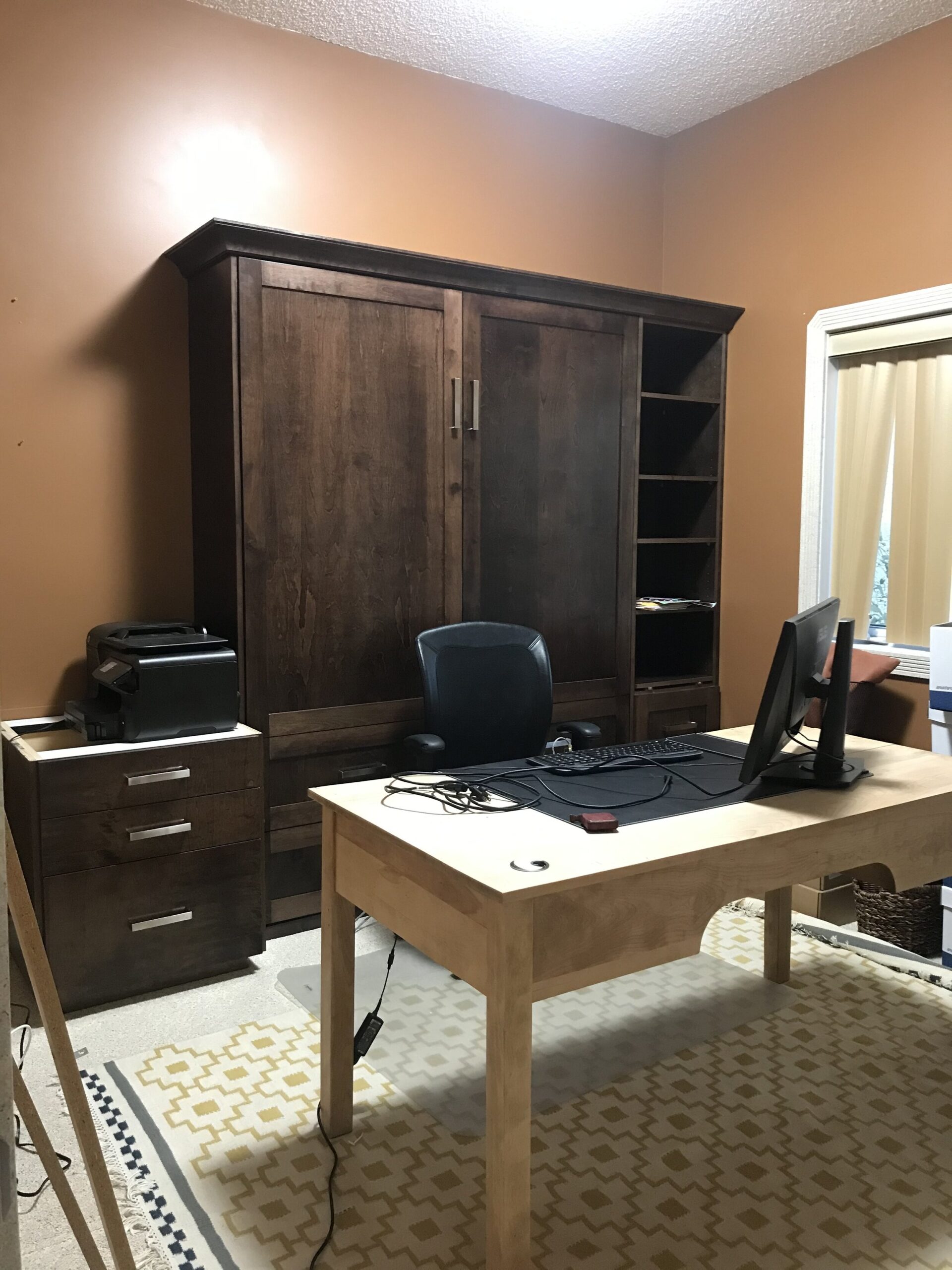 Office with built in brown wood cabinets  and wood freestanding desk in front, orange walls