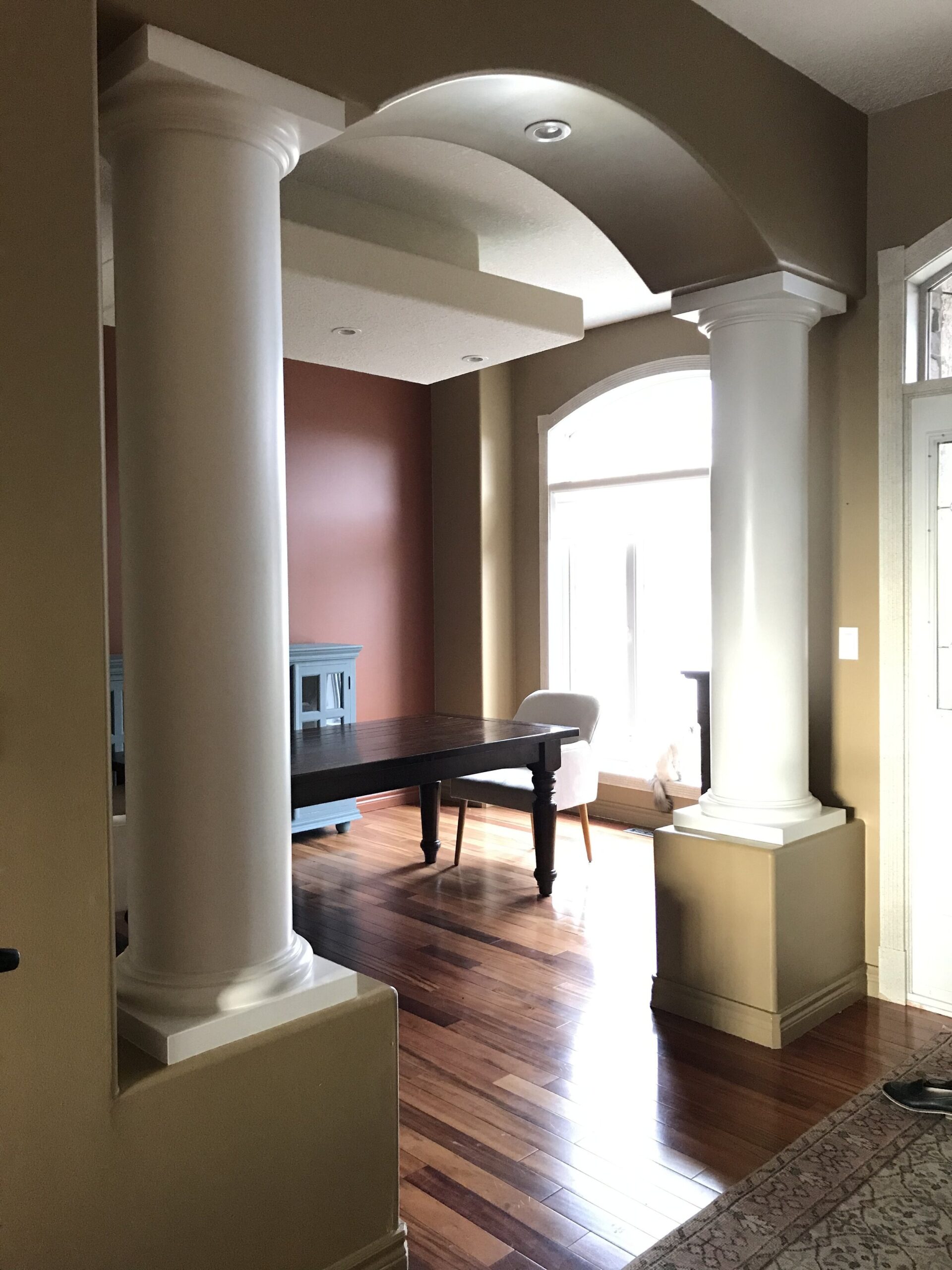 90's Modern Dining Space with red and brown walls, minimal furniture, large boxed light and columns framing the arched opening