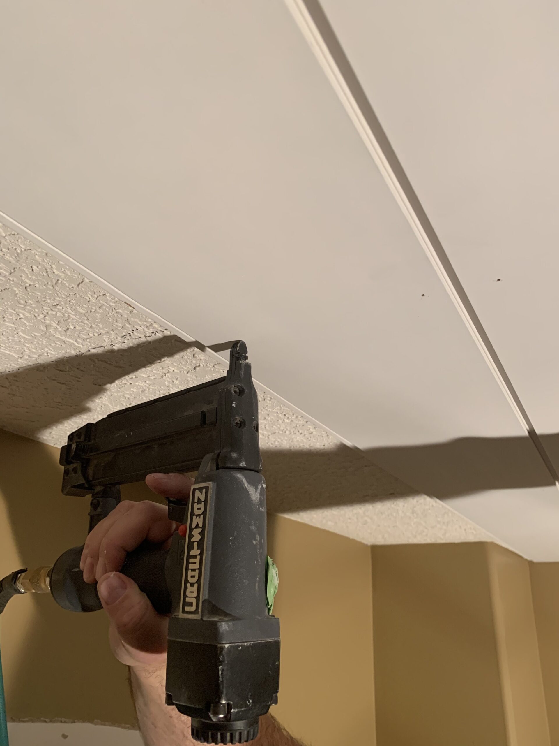 using a nail gun to shoot a nail into a shiplap board on a ceiling