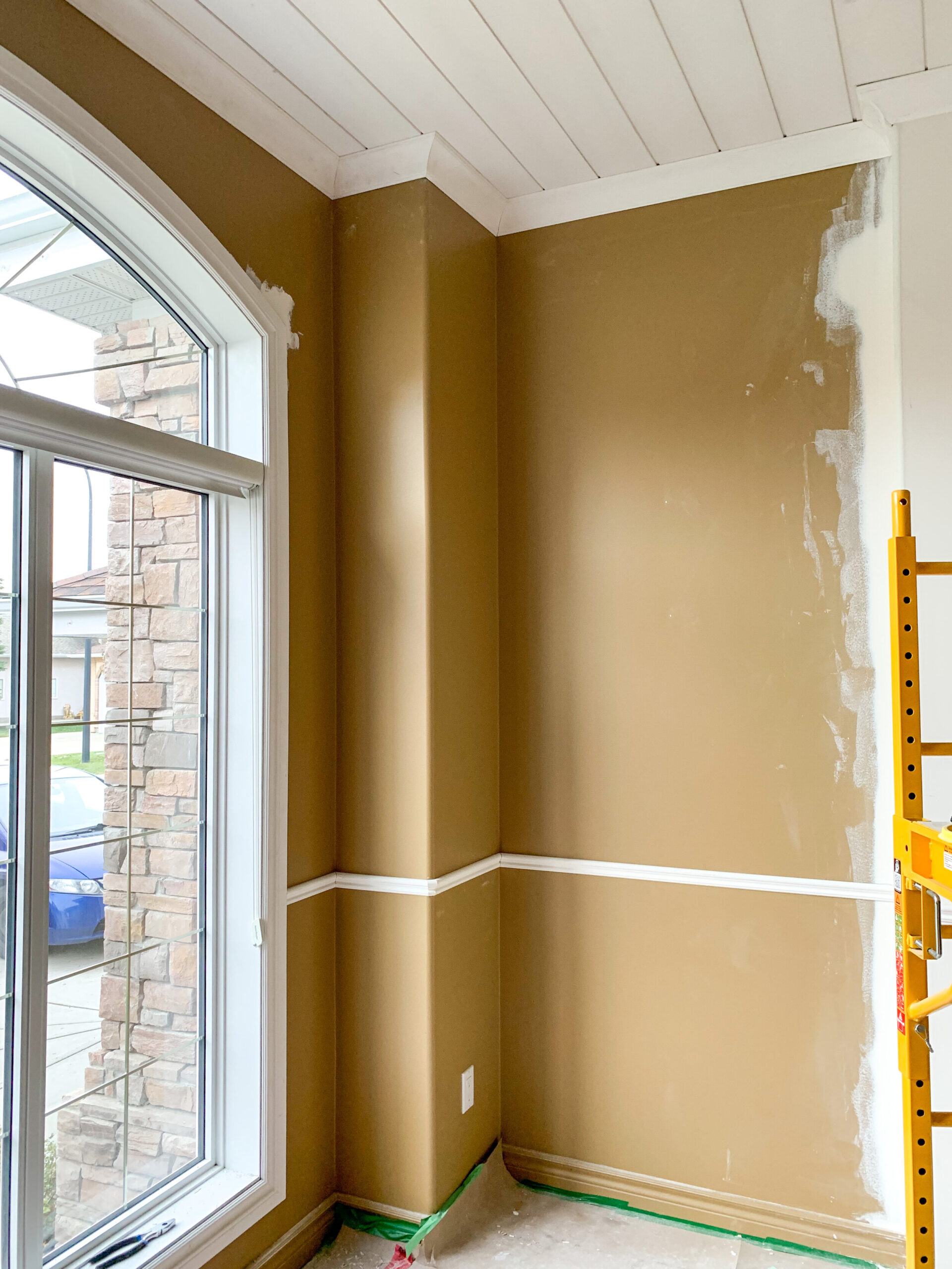 room with brown walls, some patching, shiplap ceiling and some new chair rail starting to be installed with an arched window