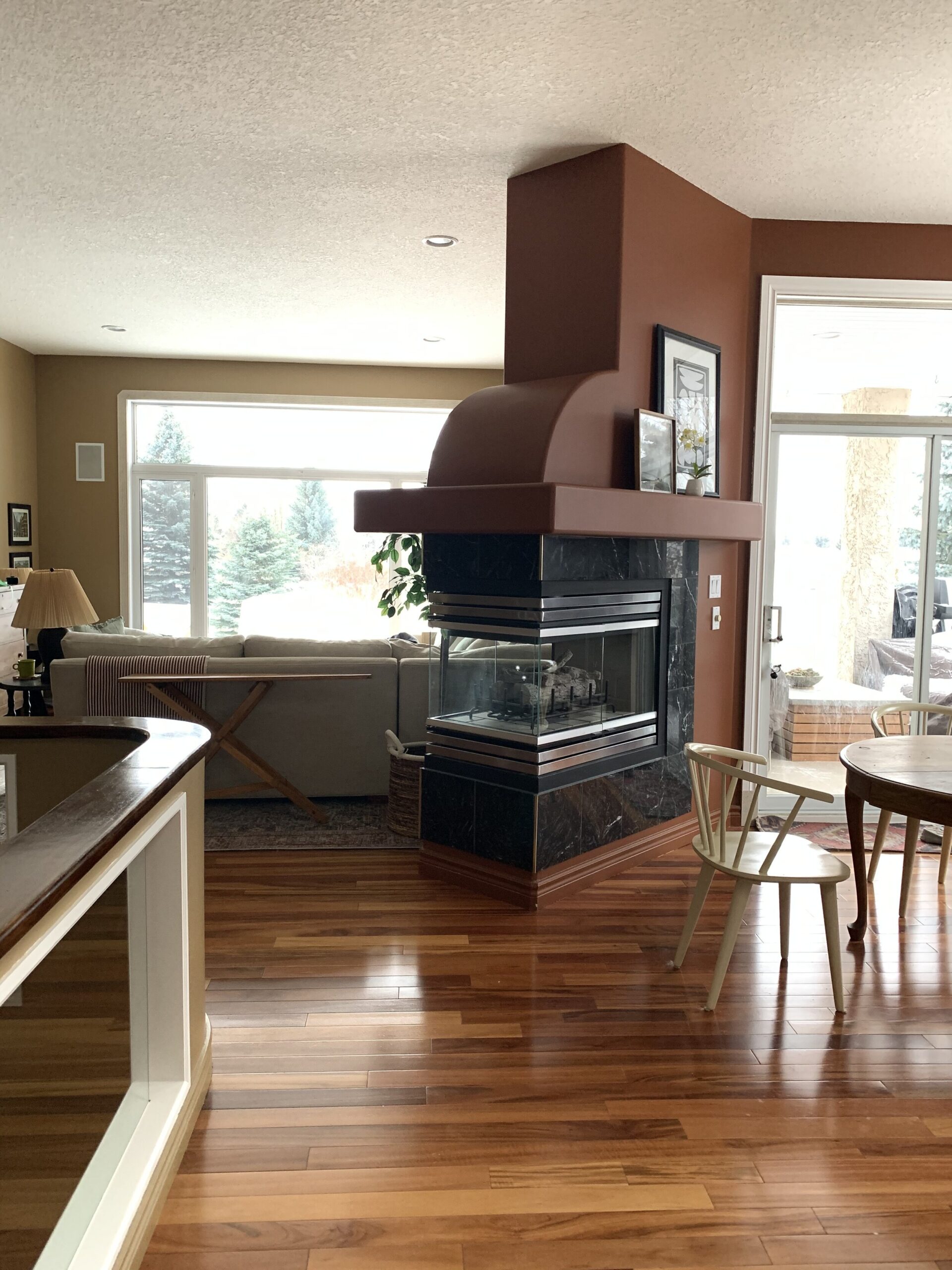 three sided angled fireplace painted brown separating a dining space from a living space