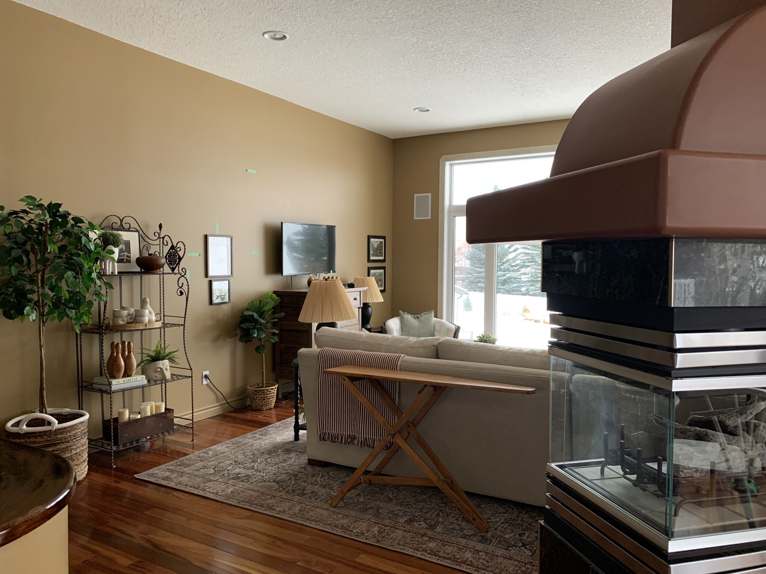 living room with brown walls and a three sided fireplace in the foreground, random furniture with a dresser and TV placed on far wall