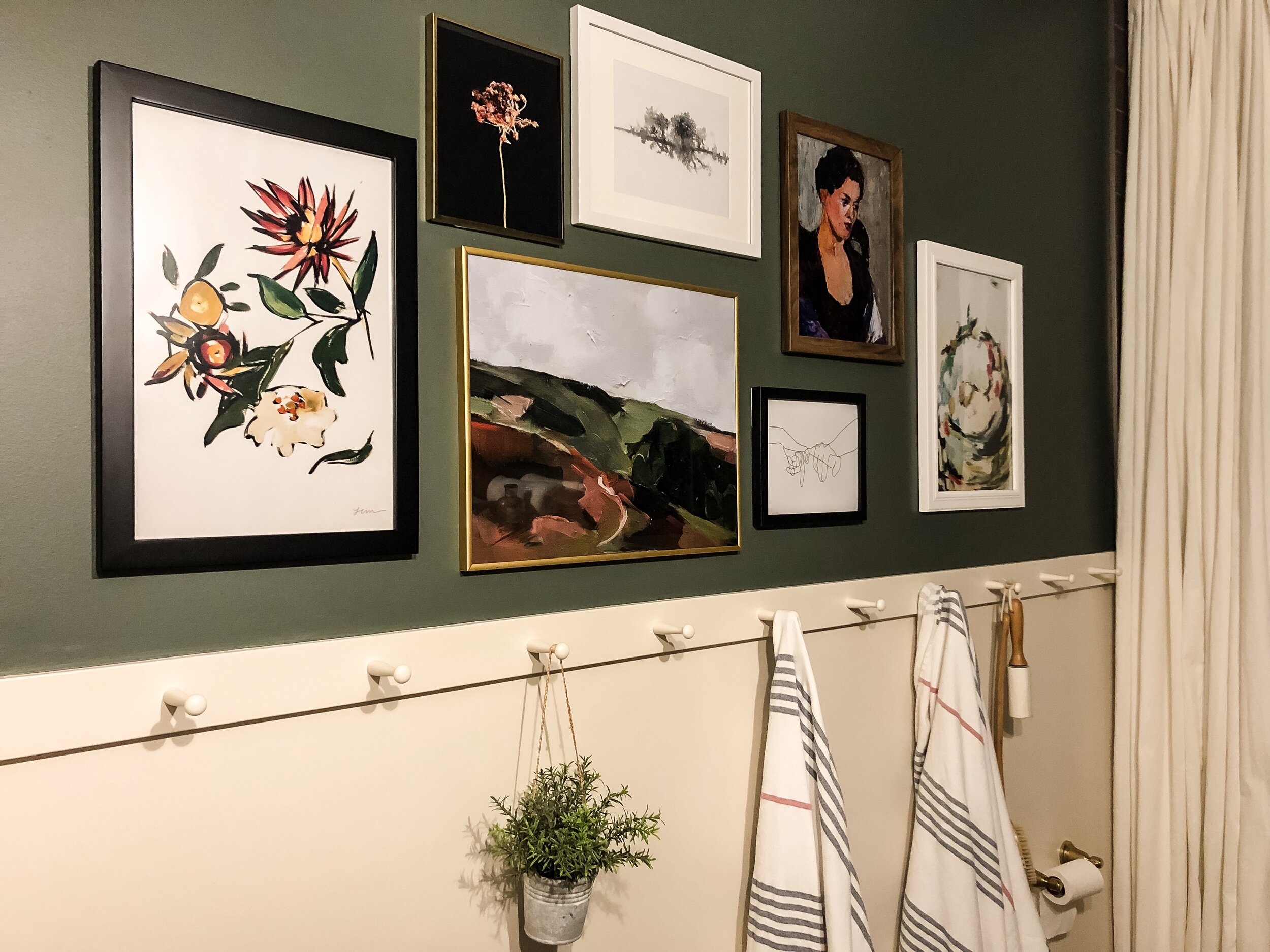 a gallery wall on a green wall with white wainscotting an peg rail with towels and a plant hanging from the peg rail.  Art is all various colours mostly from Juniper Print Shop