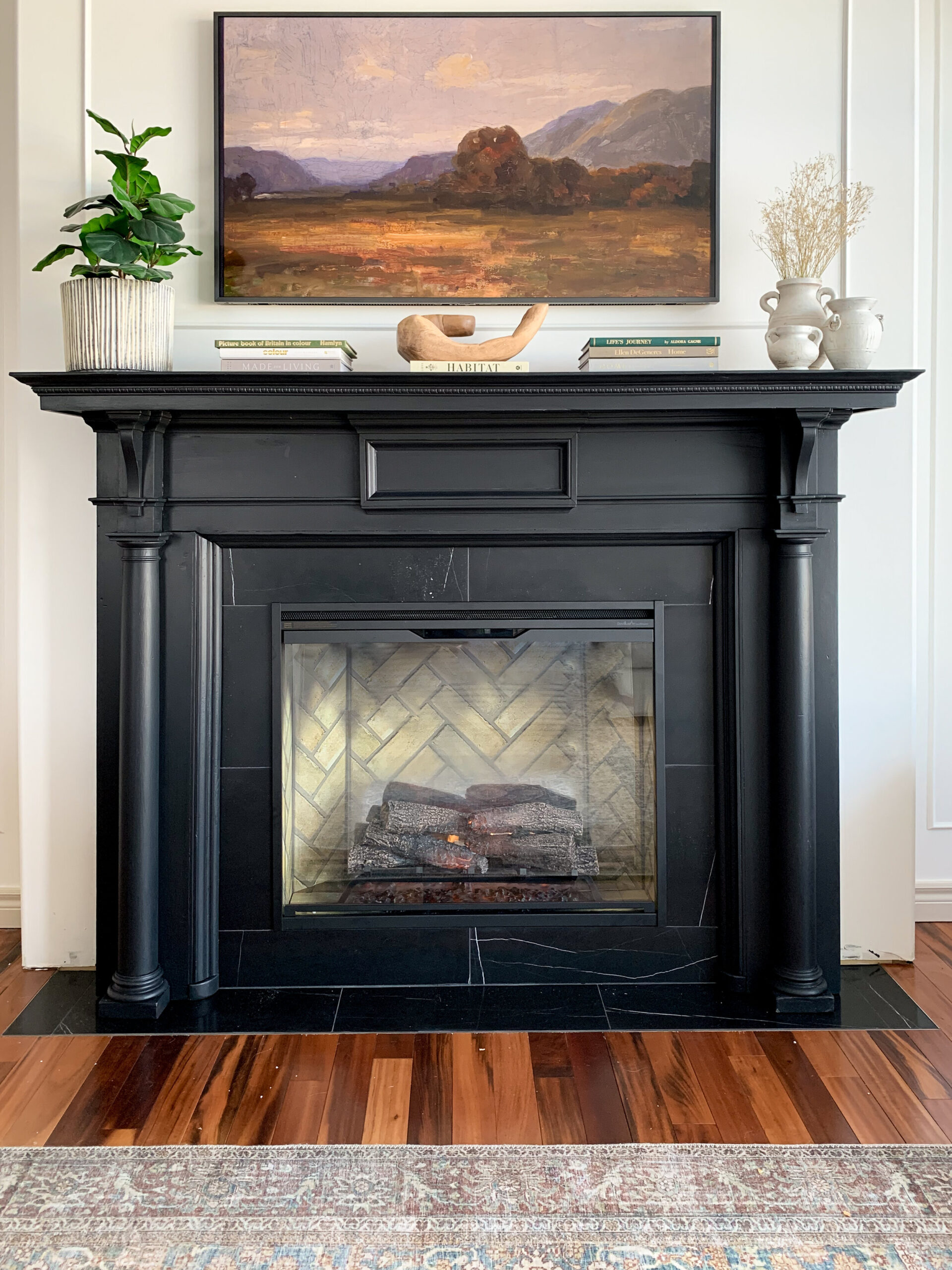 black fireplace mantle with black marble tile surround, books, plants and accessories on mantle, Frame TV above displaying art