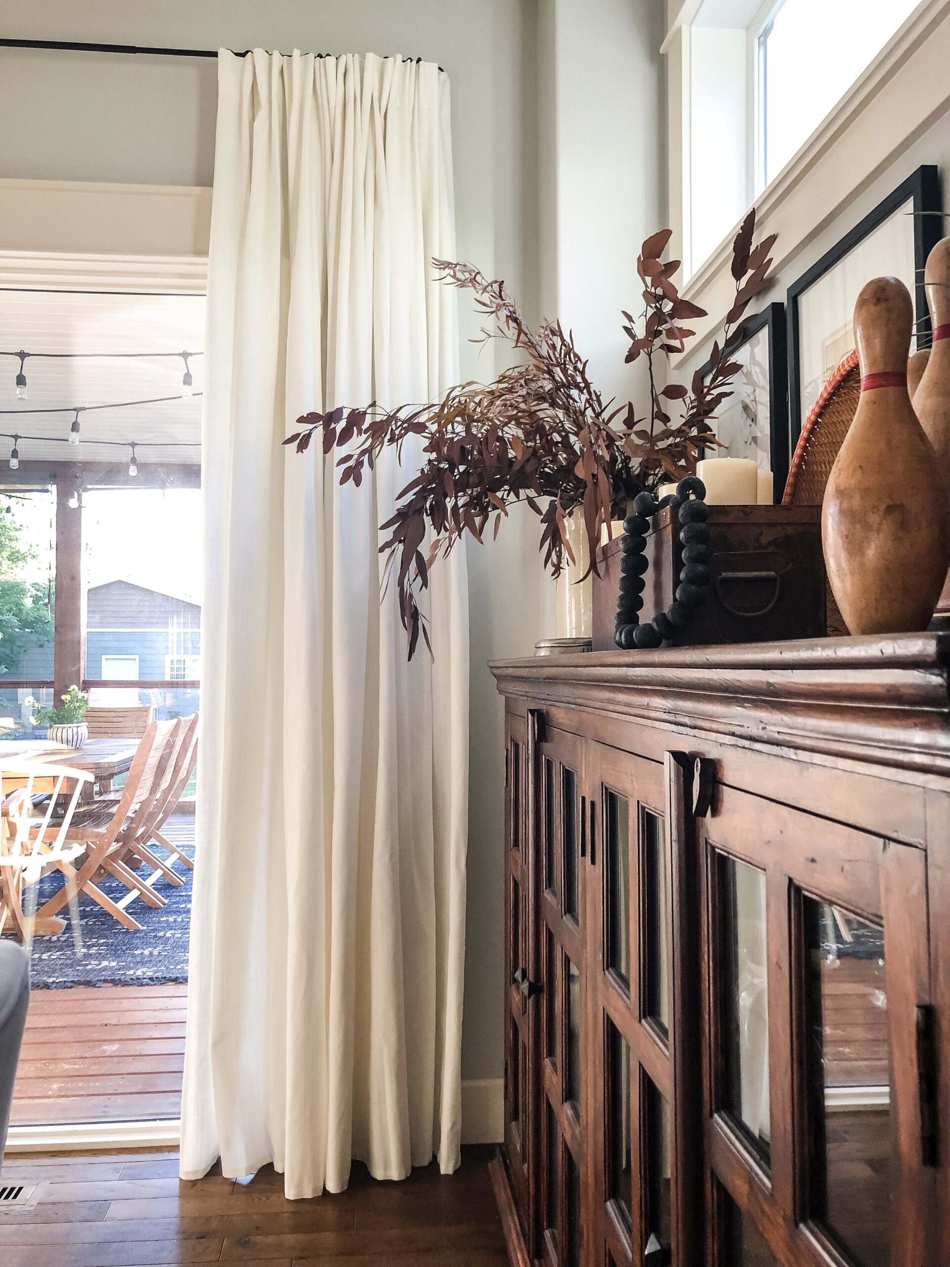 Wood sideboard with various styling items on top and curtain in the background on a window 