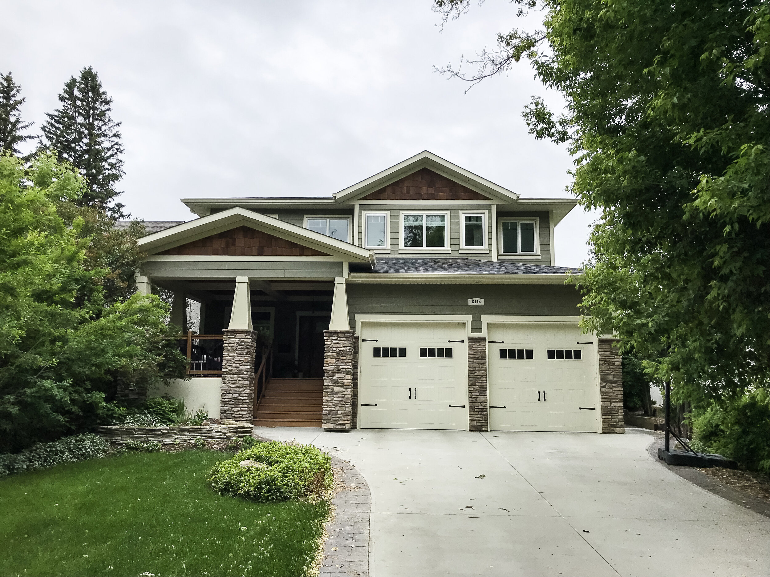 craftsman style house exterior with large front porch with stone columns, white trim and green fibre cement siding and cedar shake accents