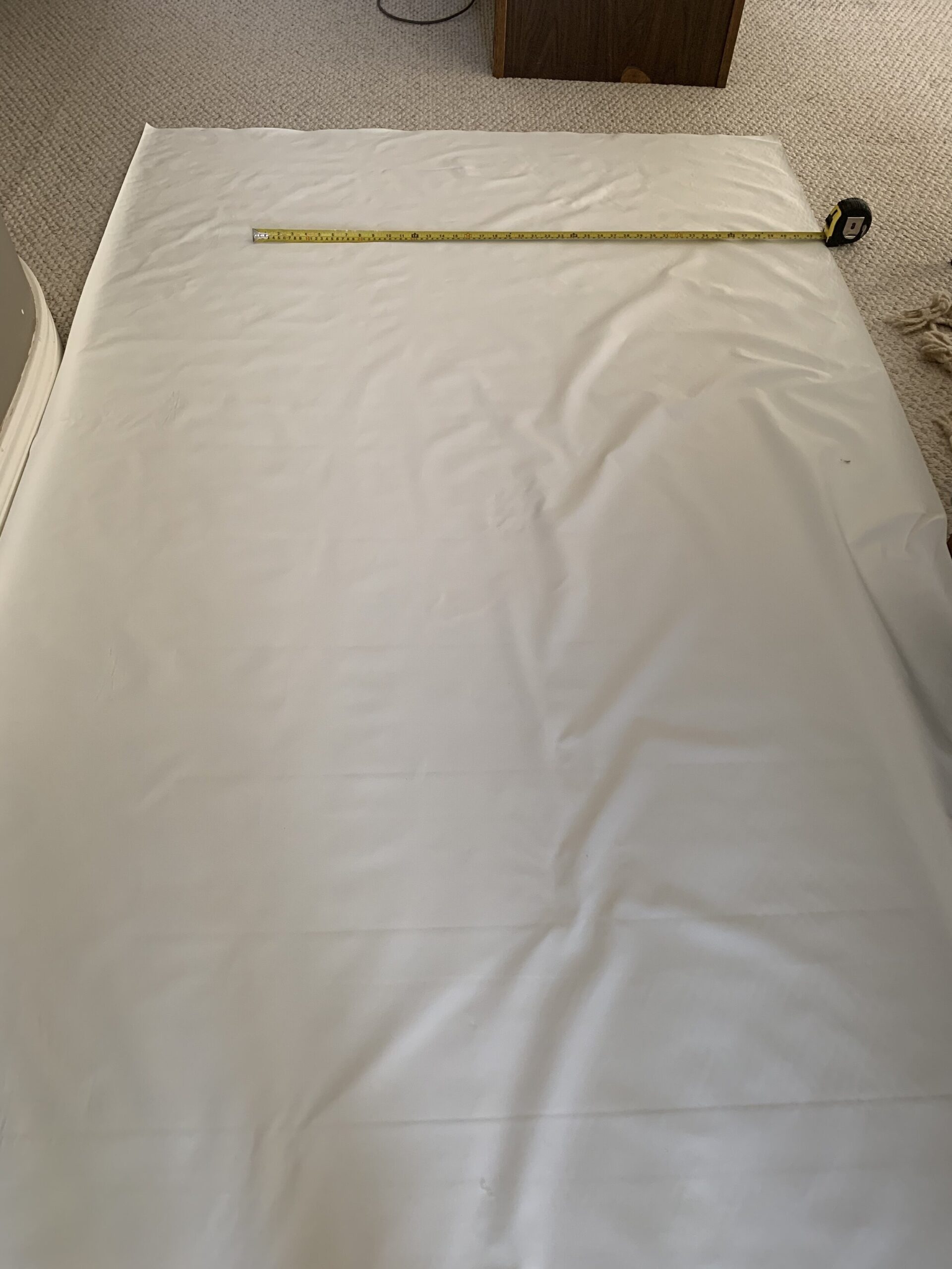 white lining fabric laying on ground and tape measure marking the width