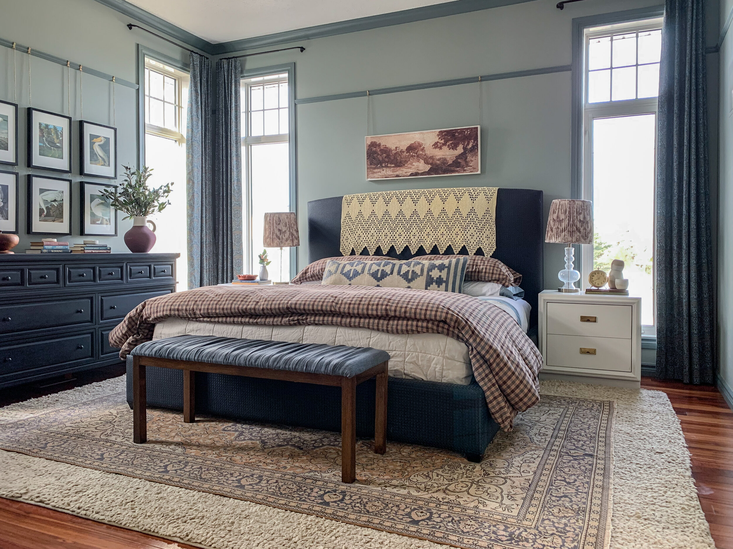 modern traditional bedroom with green walls and darker contrasting green trim, black bed and dresser, vintage rug and patterned bedding