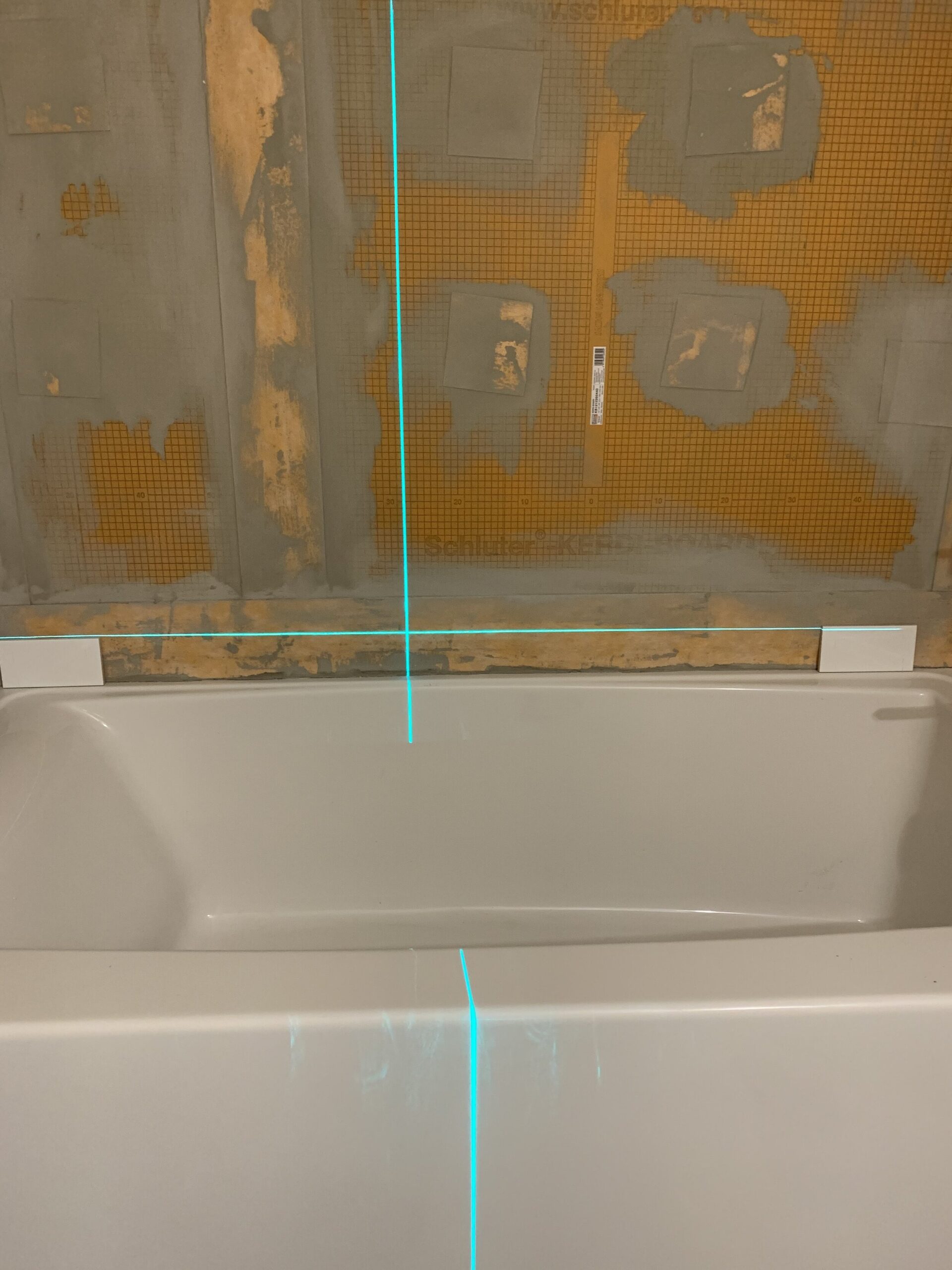 Waterproofed tub surround with laser level marking level line of bottom row of tile