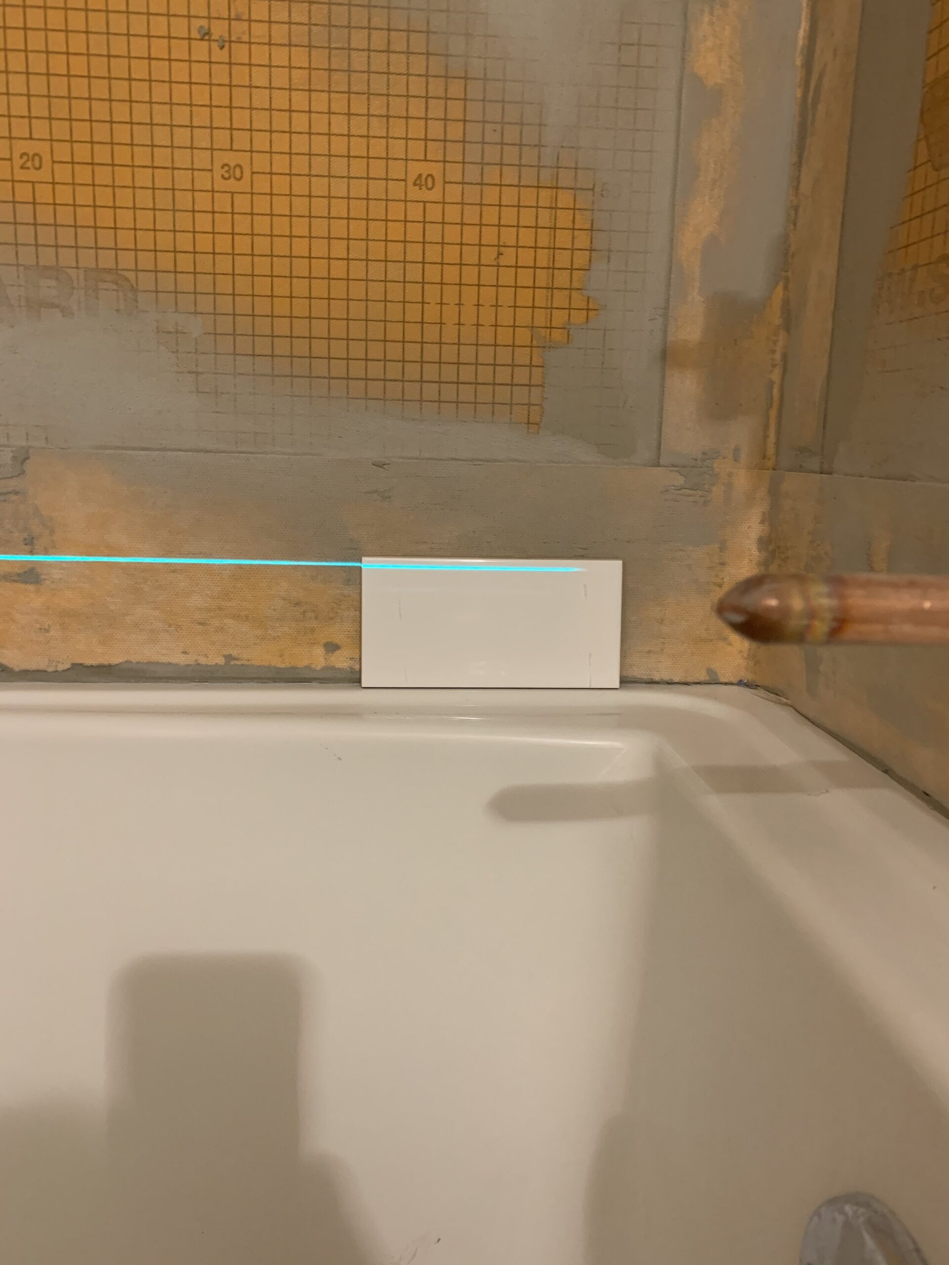 subway tile sitting on a tub edge with laser level marking the top of it