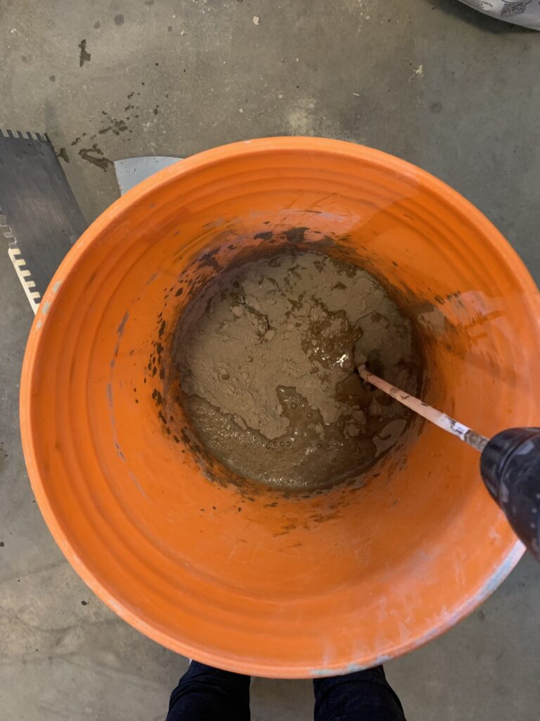 orange bucket with powdered mortar and water added and starting to mix using a drill with mix attachment