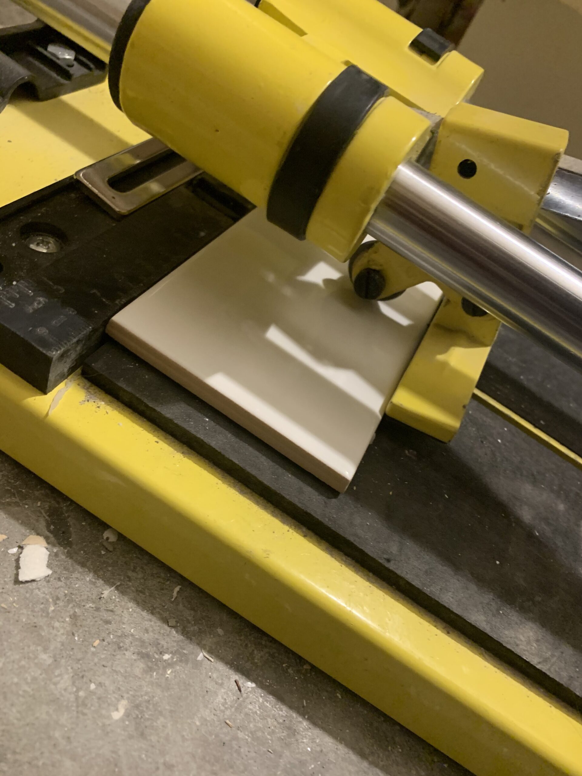using a tile cutter, scoring a subway tile with a cutting wheel