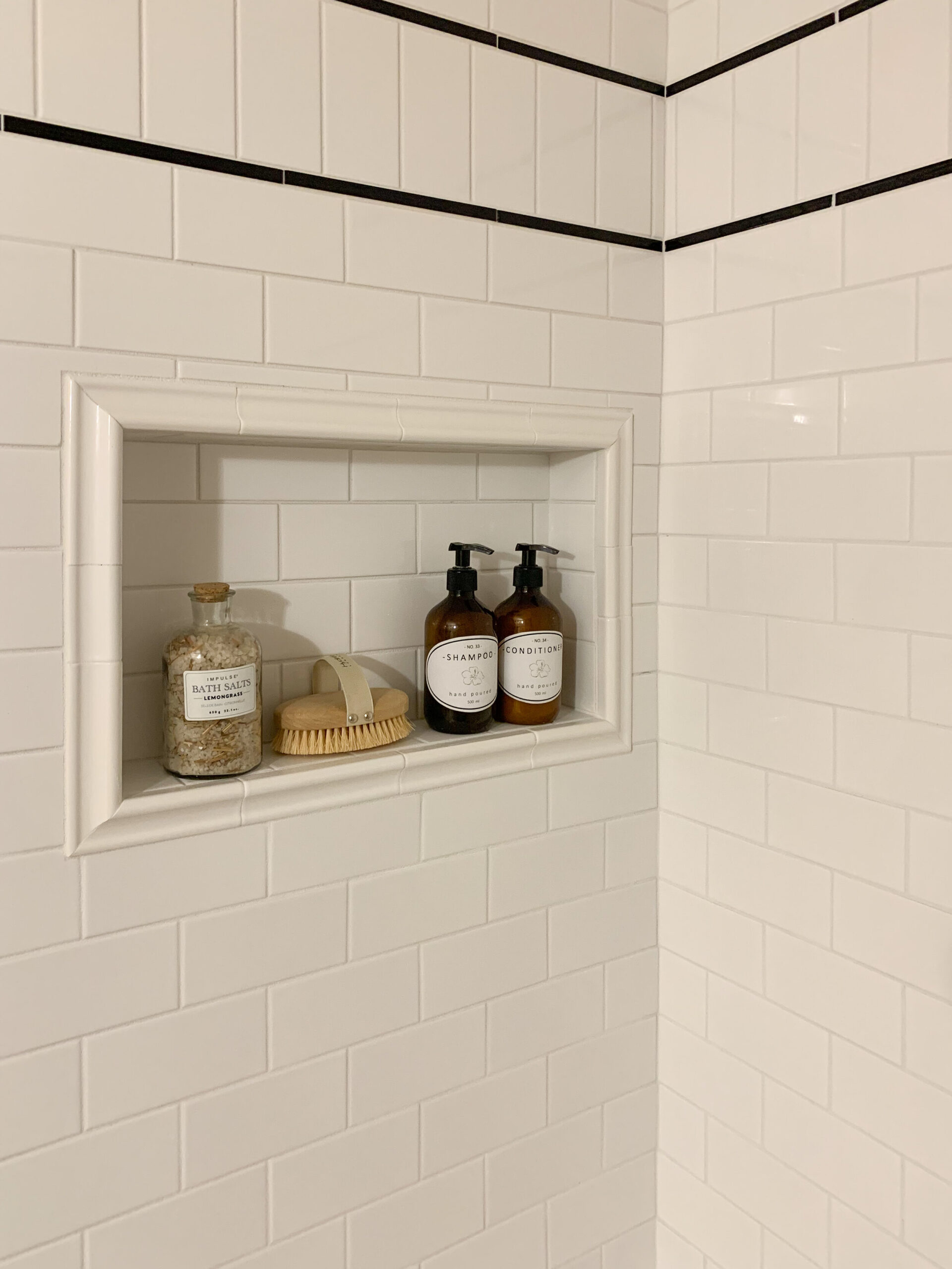 subway tile tub surround showing a shower niche framed out with bullnose tile trim and two black pencil tile trim detailed lines with subway tile turned vertically