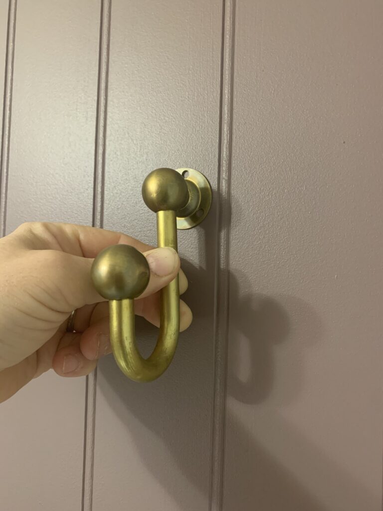 brass hook being held on a purple wall with brass aging using vinegar