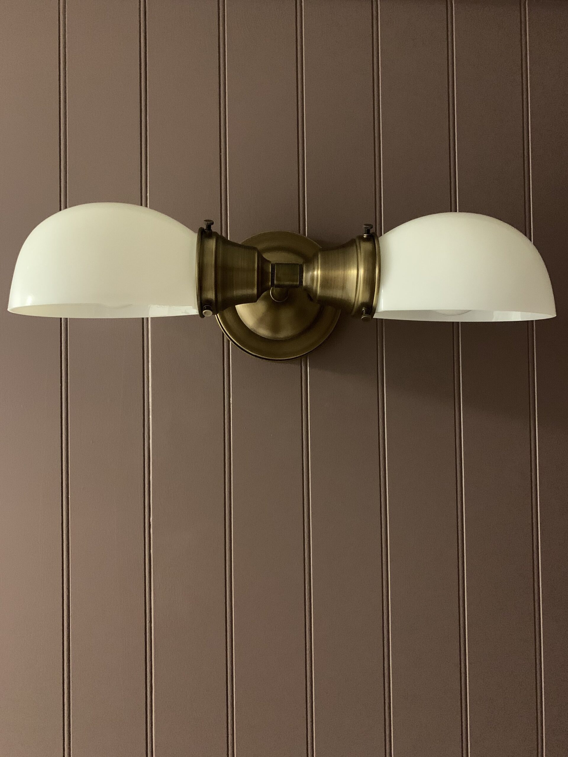 antique brass vintage style fixture with white shades on a purple beadboard wall