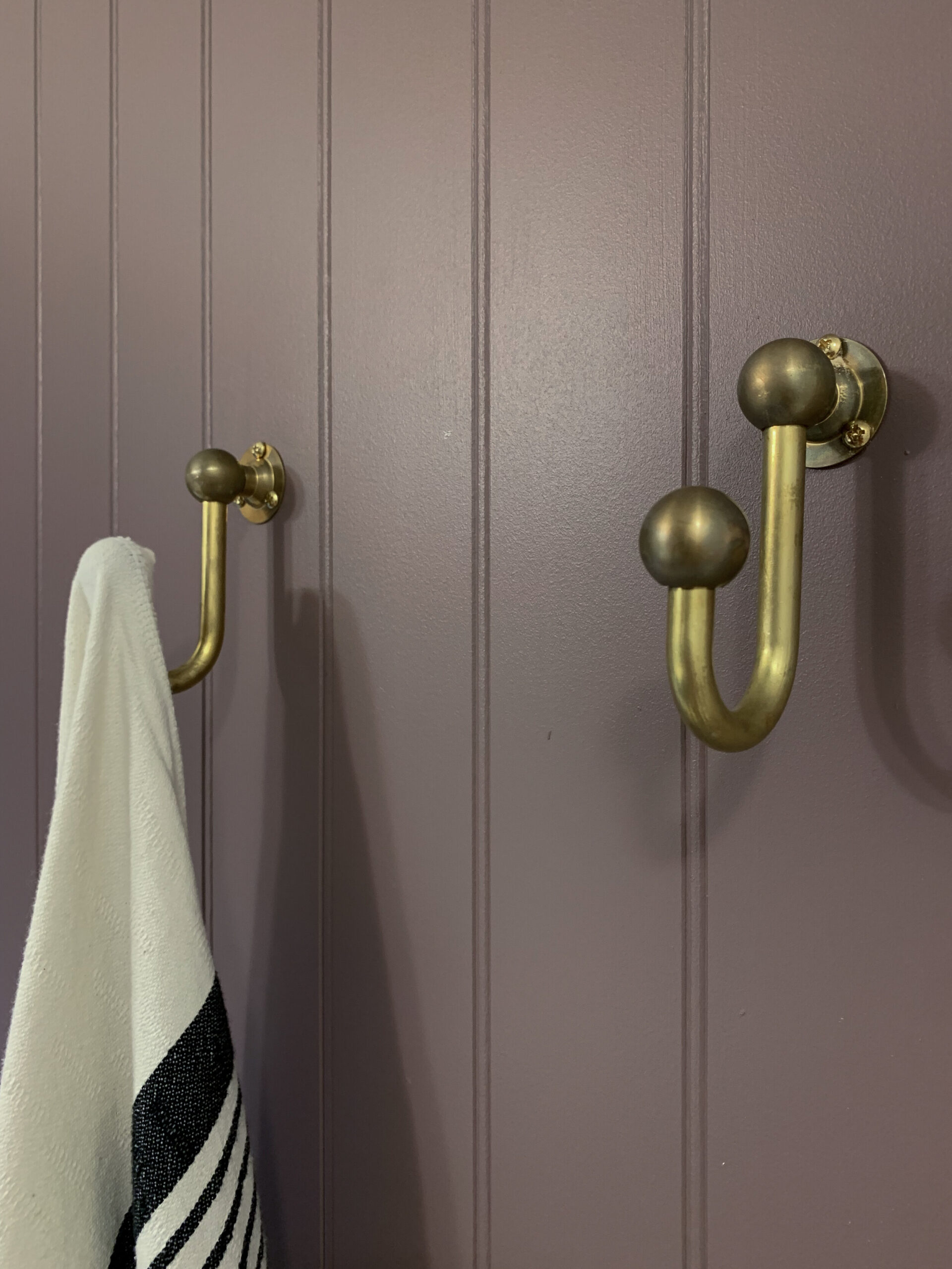 unlaquered brass hooks on a purple beadboard wall with a towel hanging on one hook