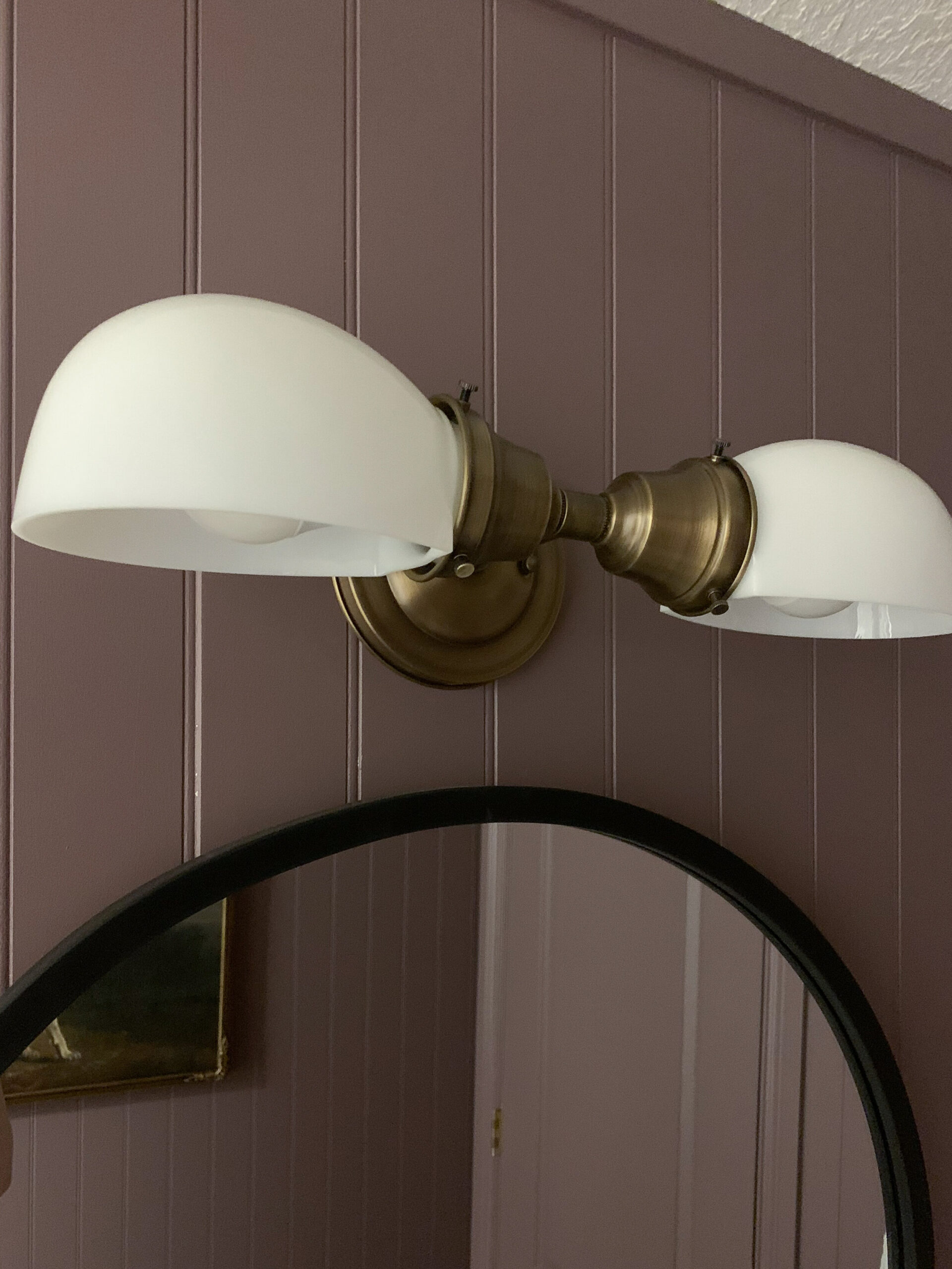 aged brass two bulb vintage style light with a black arch mirror below on a purple wall