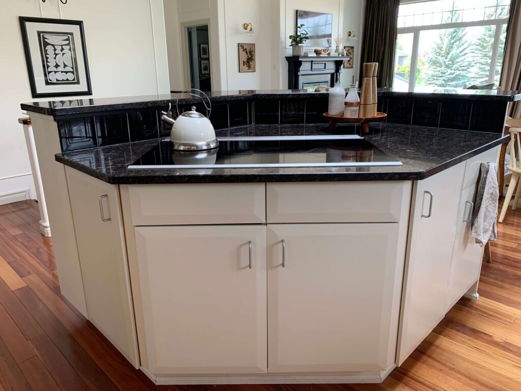 Angled kitchen island showing an induction range taking up the entire countertop , whiche flat front cabinets and raised eating bar