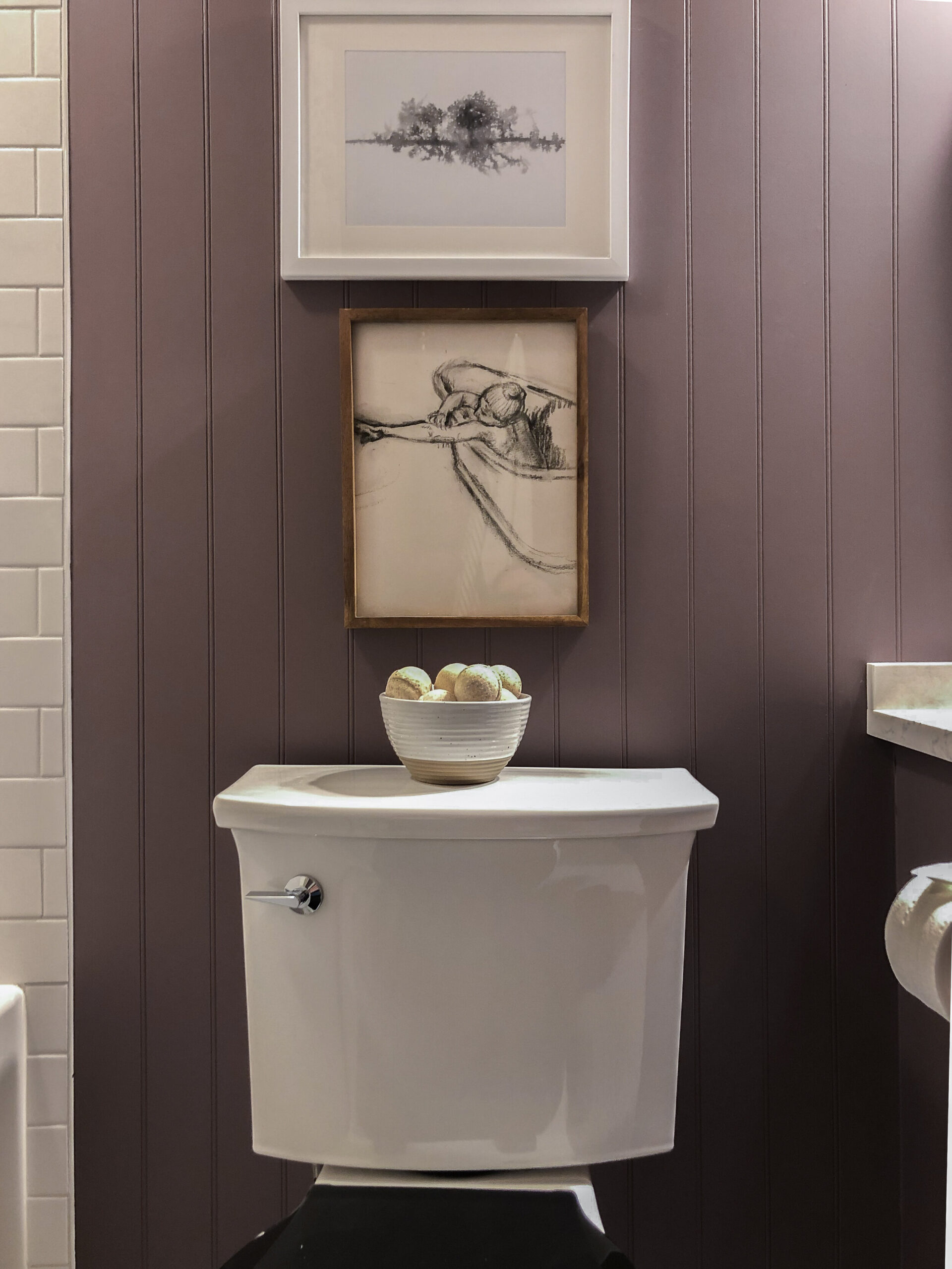 Purple beadboard walls behind a toilet with stacked art featuring a Degas sketch and abstract art