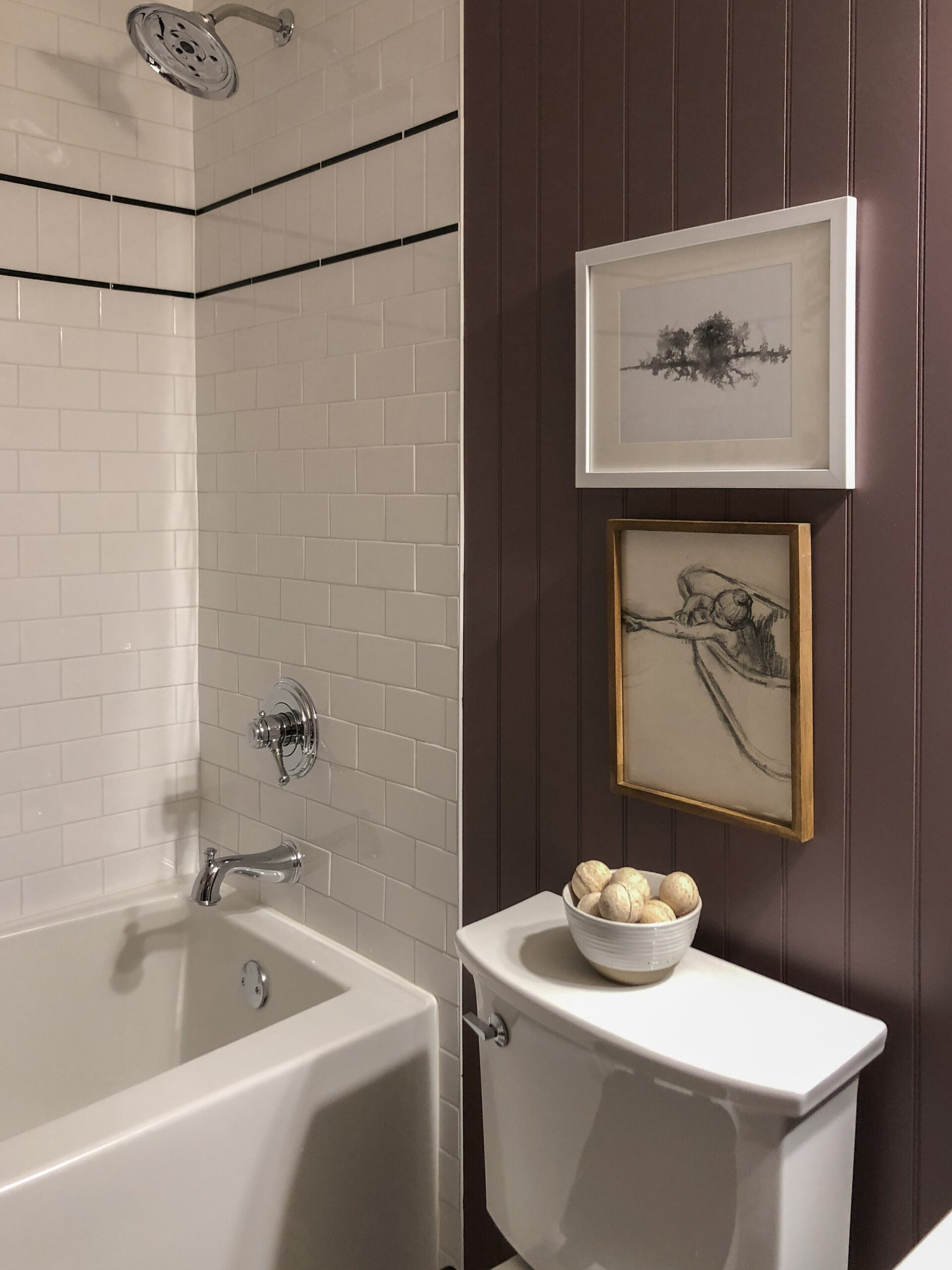 bathroom with new tub, white subway tile with black accents, purple beadboard walls and art stacked over toilet