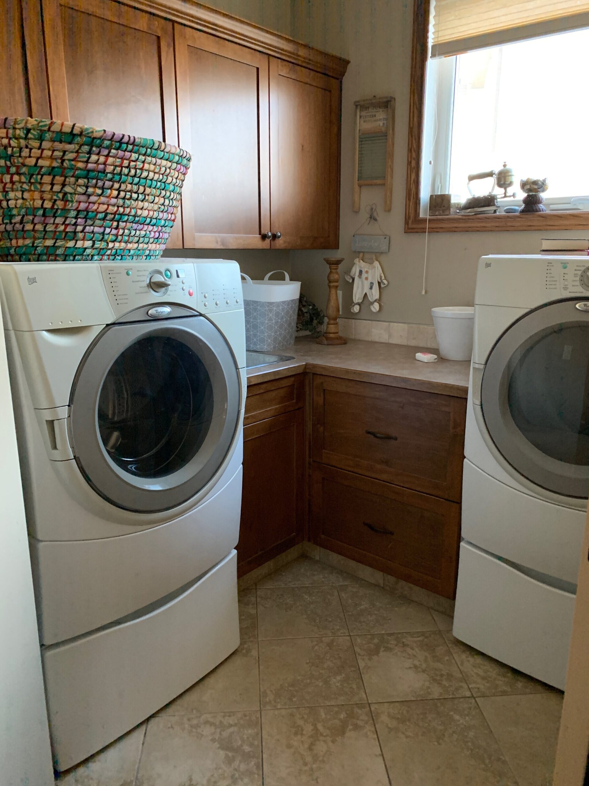 laundry room with brown wood cabinets, brown walls, brown lino counters, brown tile floor, a window and a washer dryer
