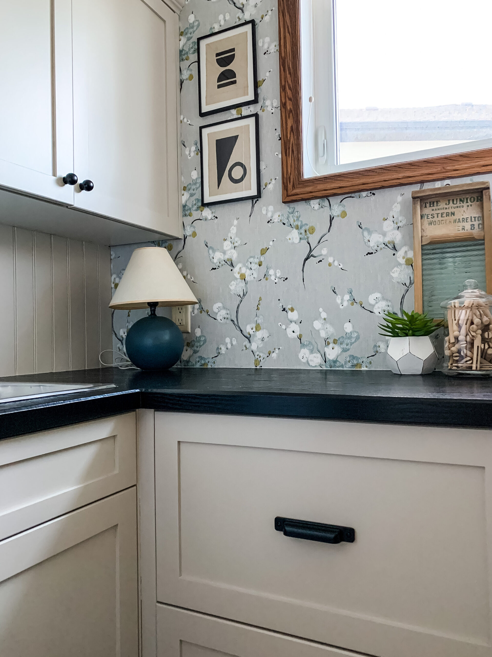 beige cabinets with black counters, floral grey wallpaper, small blue lam, modern art, some styling pieces on counter