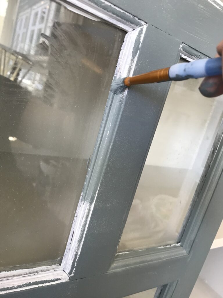 painging the edge of a furniture piece blue with a very small brush up against glass