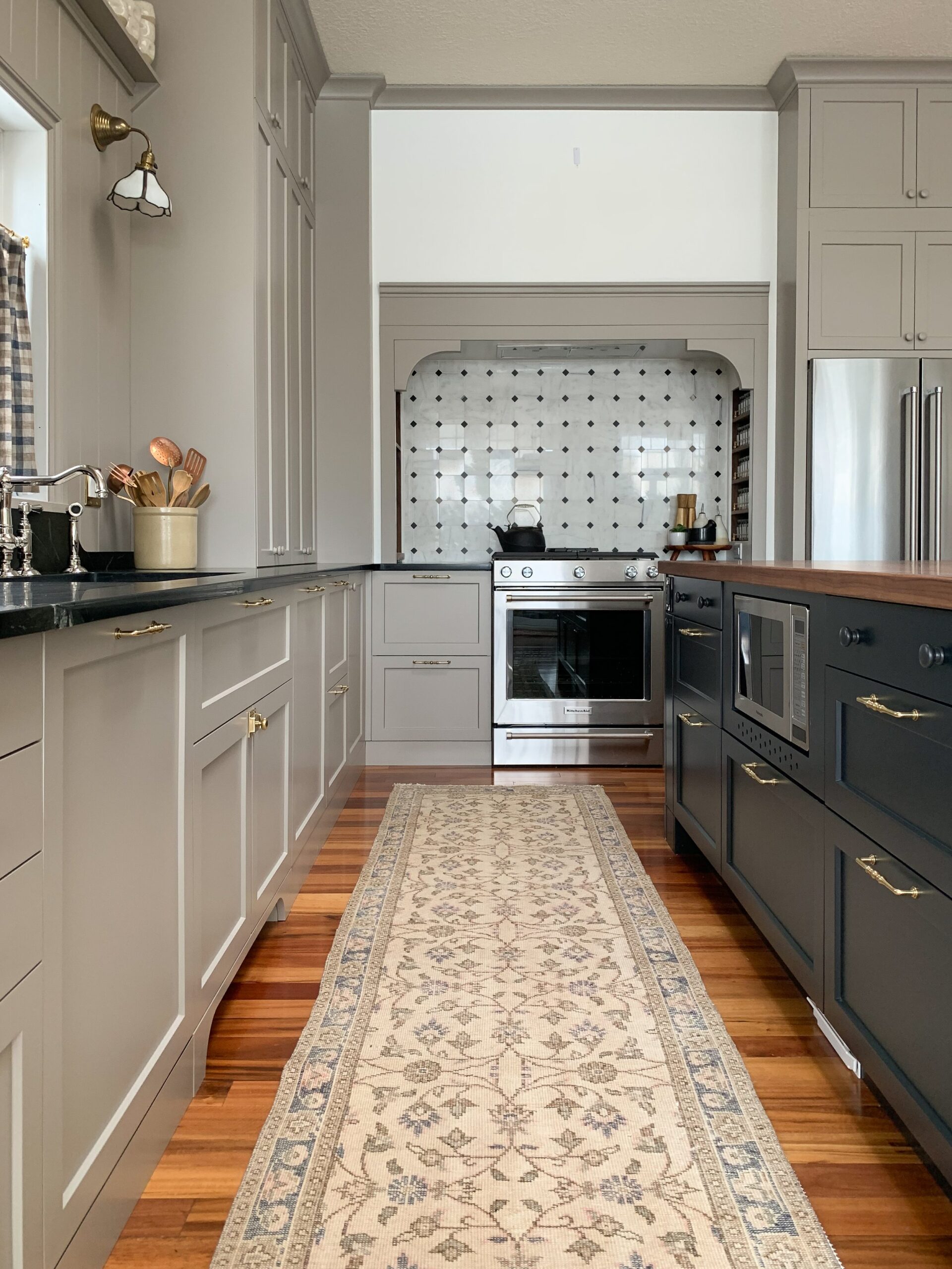 Custom Range Hood in a kitchen with beige perimeter cabinets and black island, vintage runner and marble tile