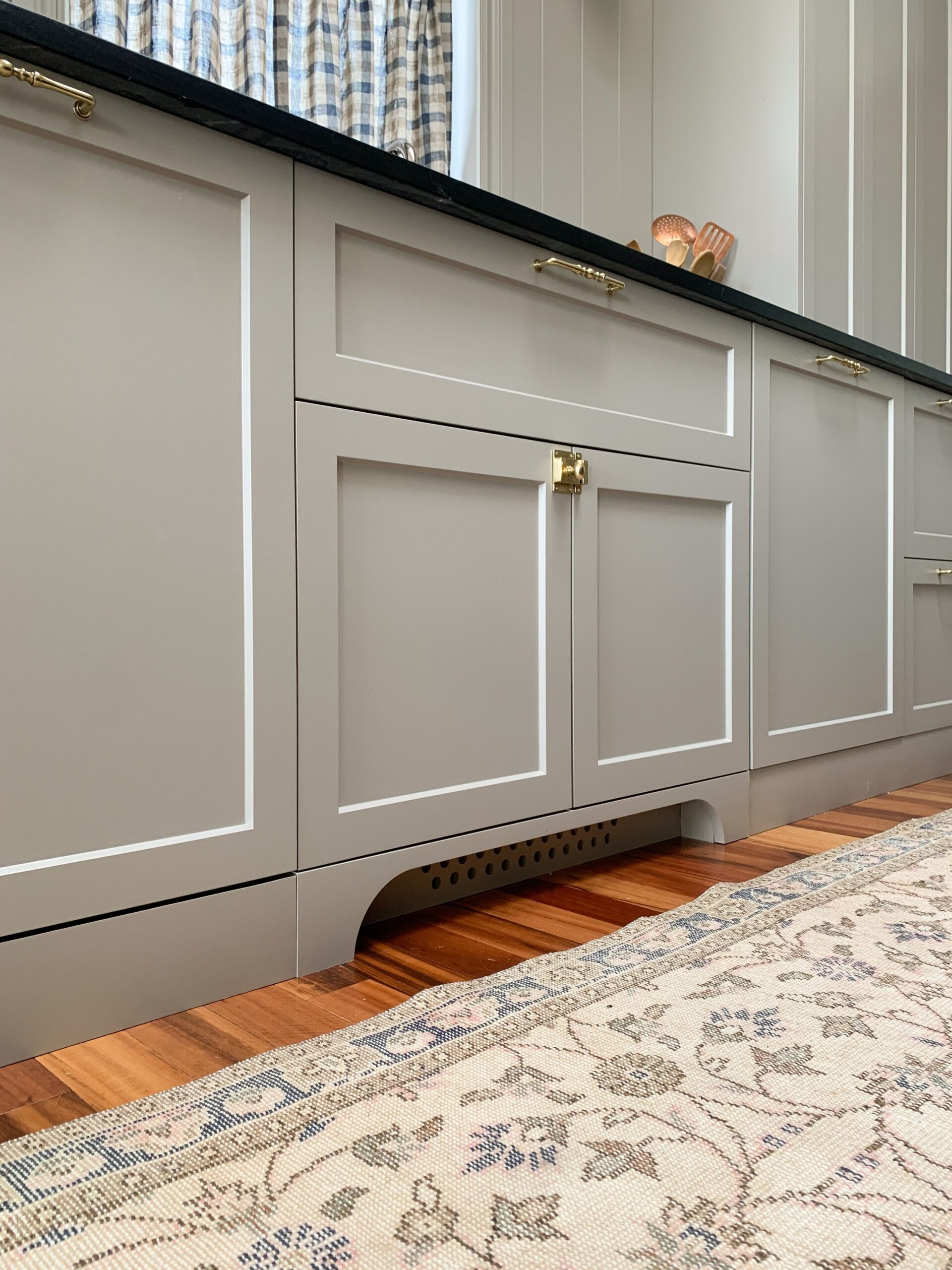 Arched toe kick in front of sink wtih vent holes cut in toe kick behind the arch, beige cabinets, vintage rug