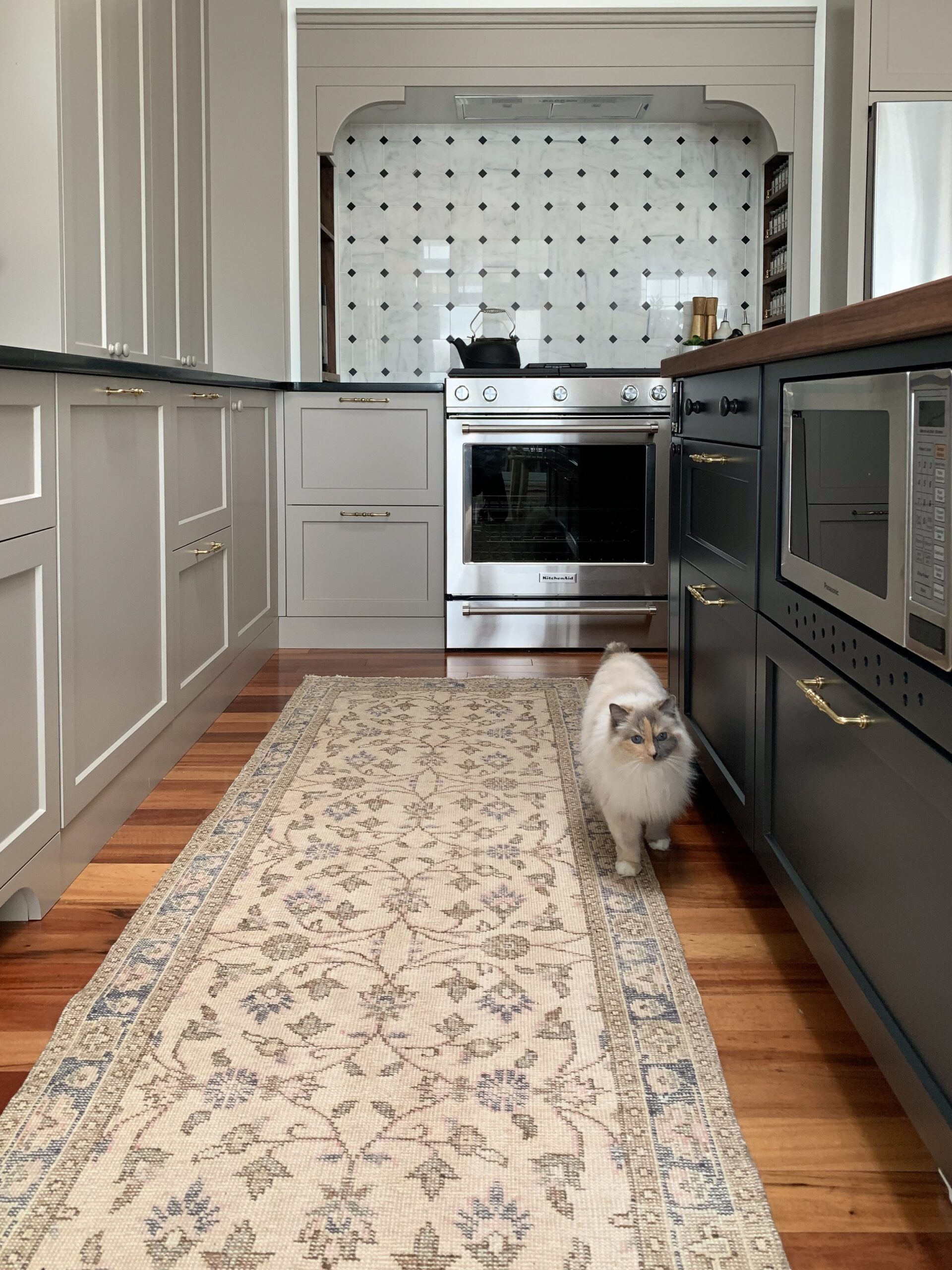 Modern Traditional kitchen with beige cabinets, black island, vintage runner, and marble backsplash, and a cat