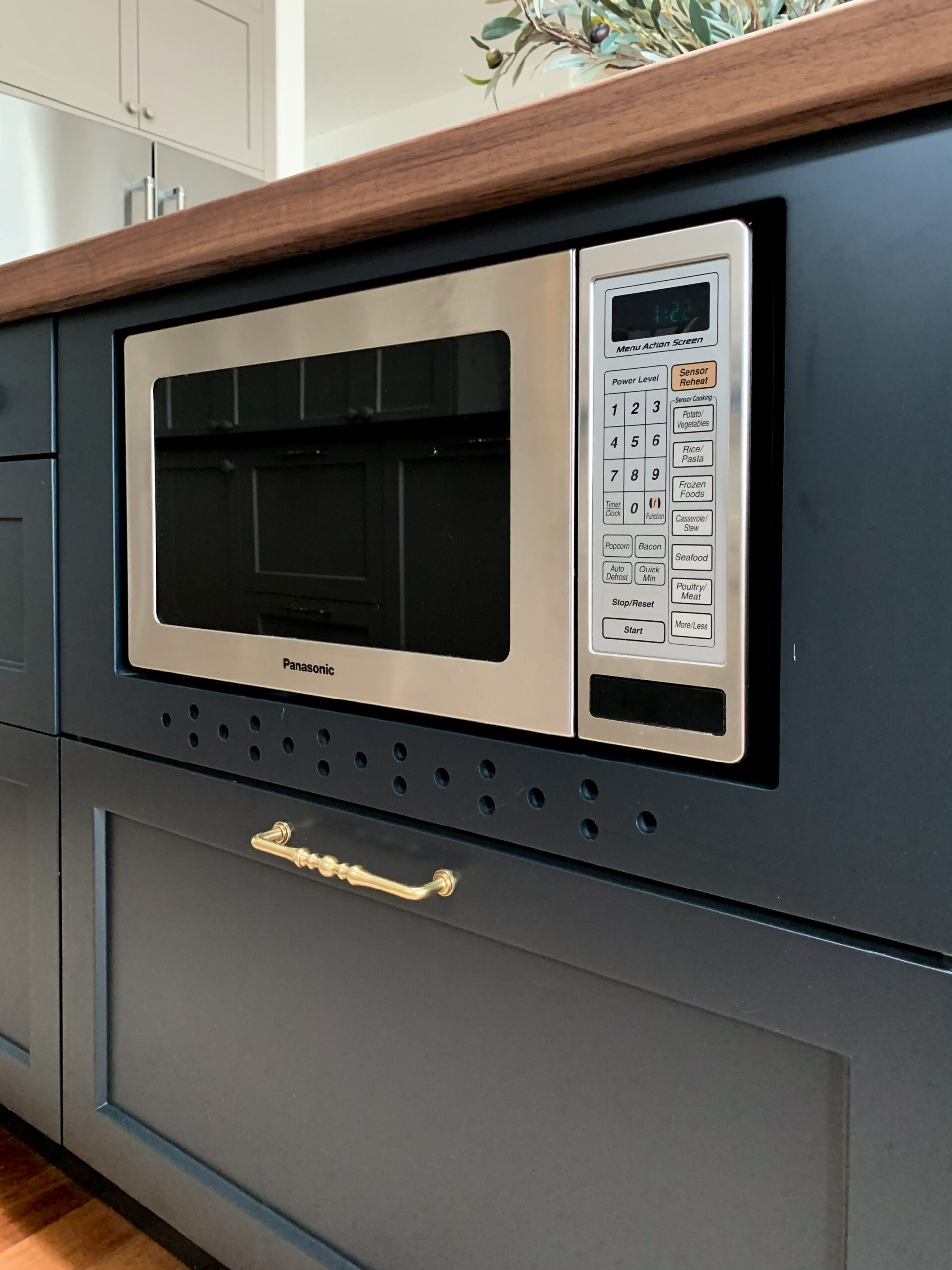 Microwave with custom vent cover with small vent holes in black island under countertop
