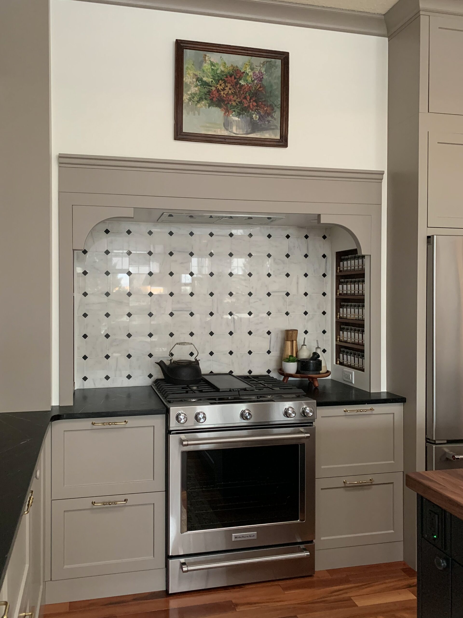 Stove Nook showing a built in custom range hood with beige cabinets, marble tile backsplash and kitchenaid stove