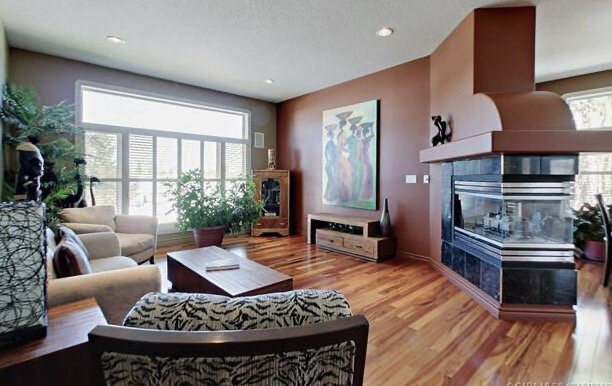 living room with angled three sided fireplace, brownish red walls, large window with shutters and wood floors