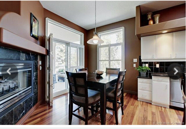 dining nook with patio doors and large window with three sided fireplace on one side and kitchen cabinets on the other